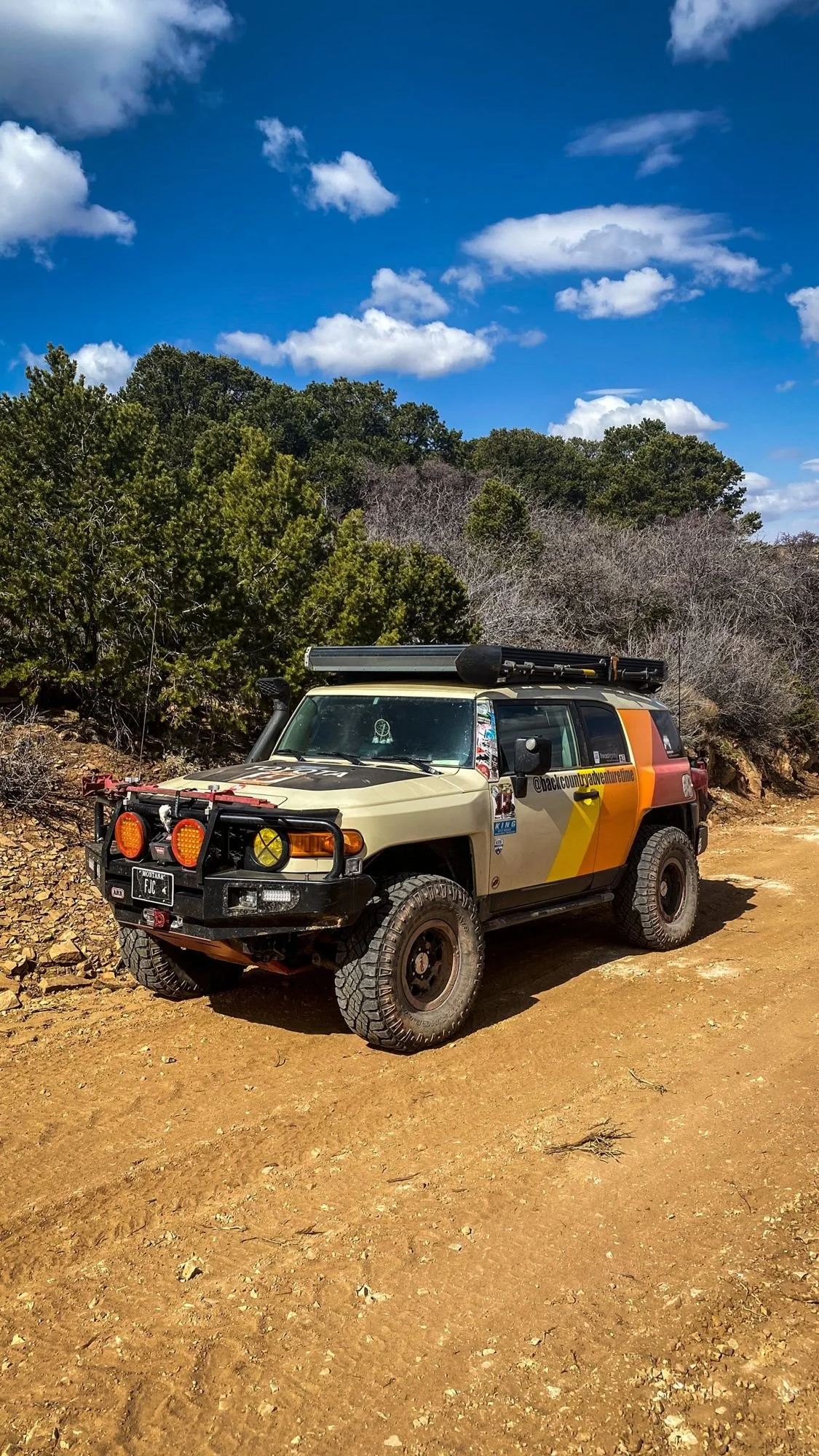 FJ Cruiser on a sandy trail with junipers and puffy clouds on a spring road trip through Utah