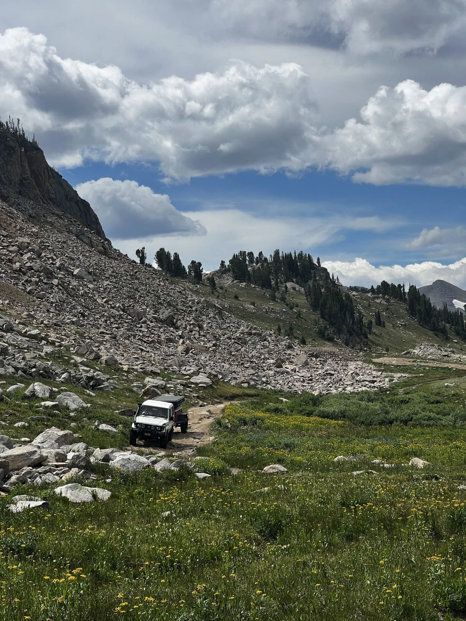 Small white truck crossing a wide alpine basin below a boulder field and peaks near Cooke City, Montana