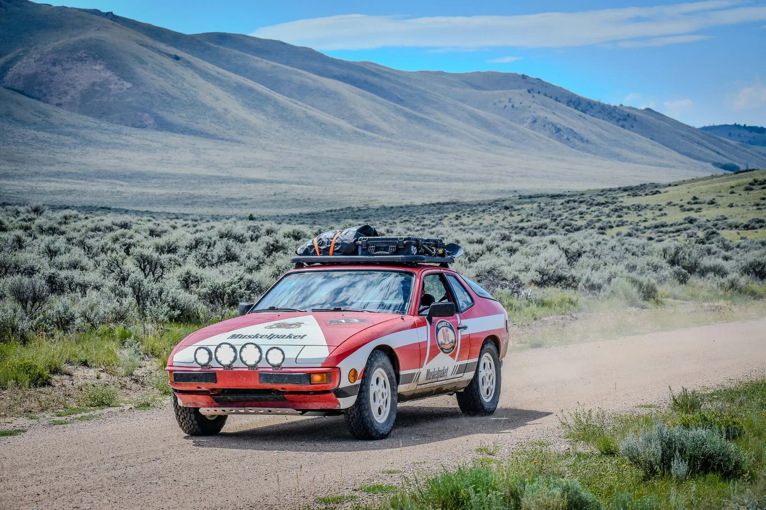 Red Porsche 944 rally car driving across open Montana sagebrush country