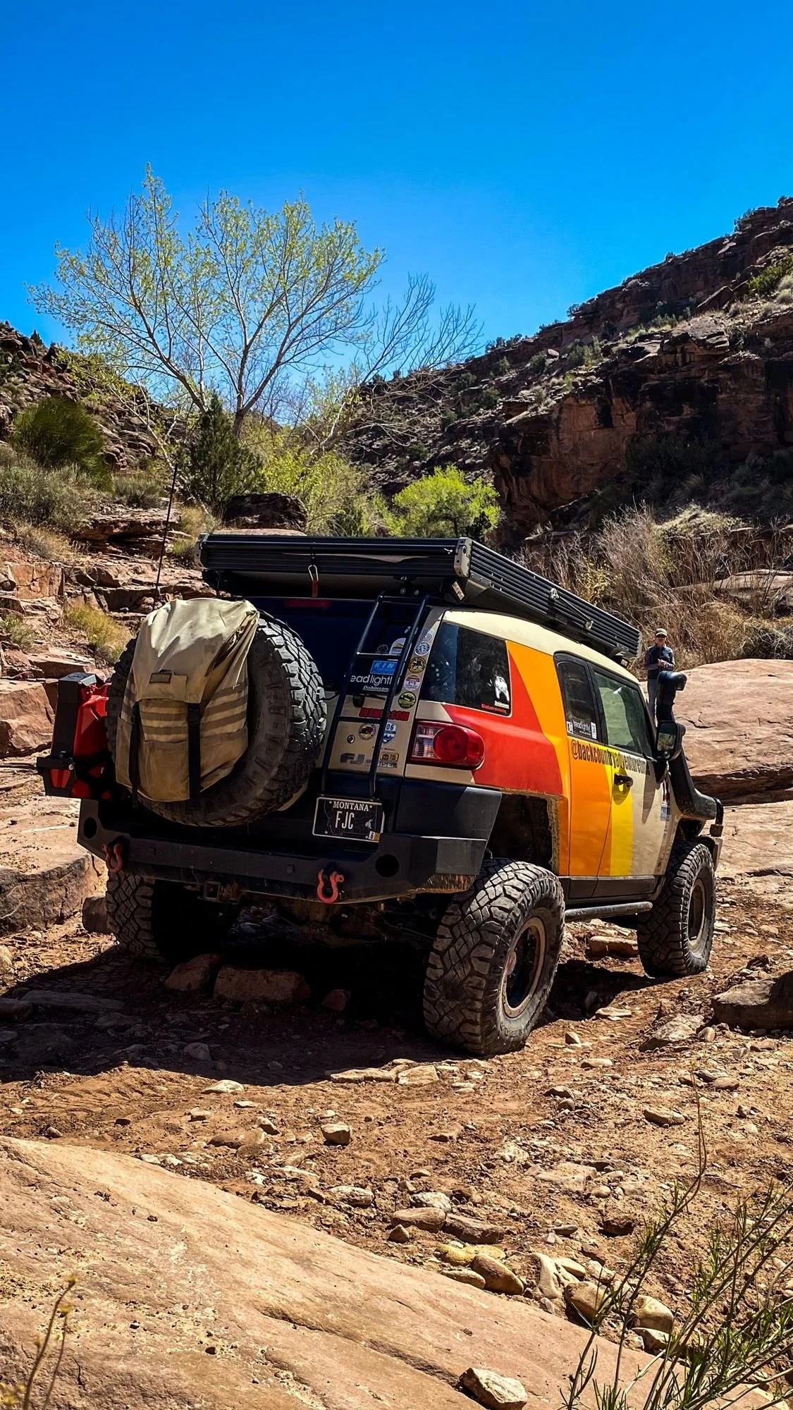 Striped FJ Cruiser with a rear tire bag in a sandstone wash below cliffs on a spring road trip through Utah