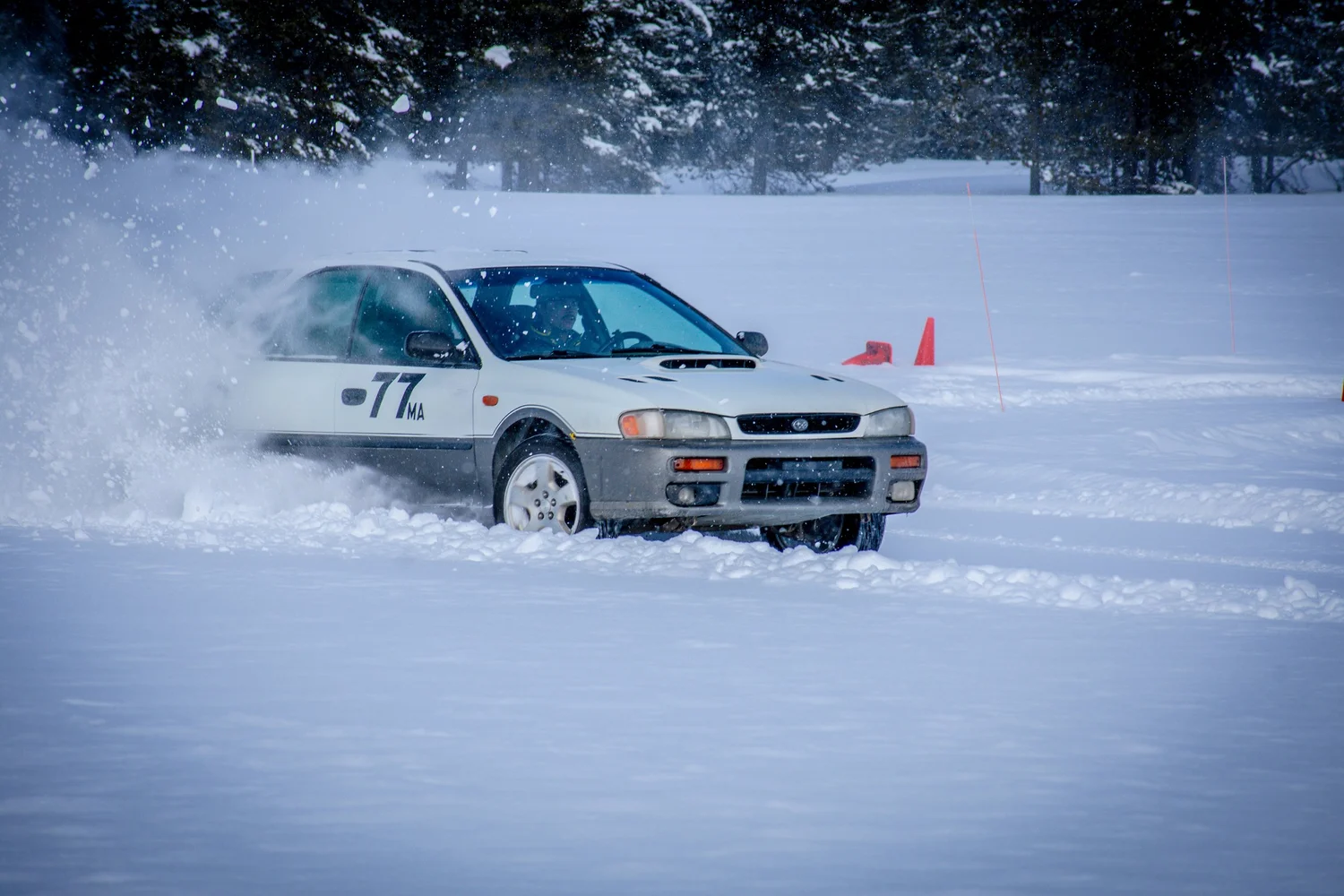 White Subaru Impreza rally car number 77 sliding through snow at the Frost and Furious ice races in West Yellowstone