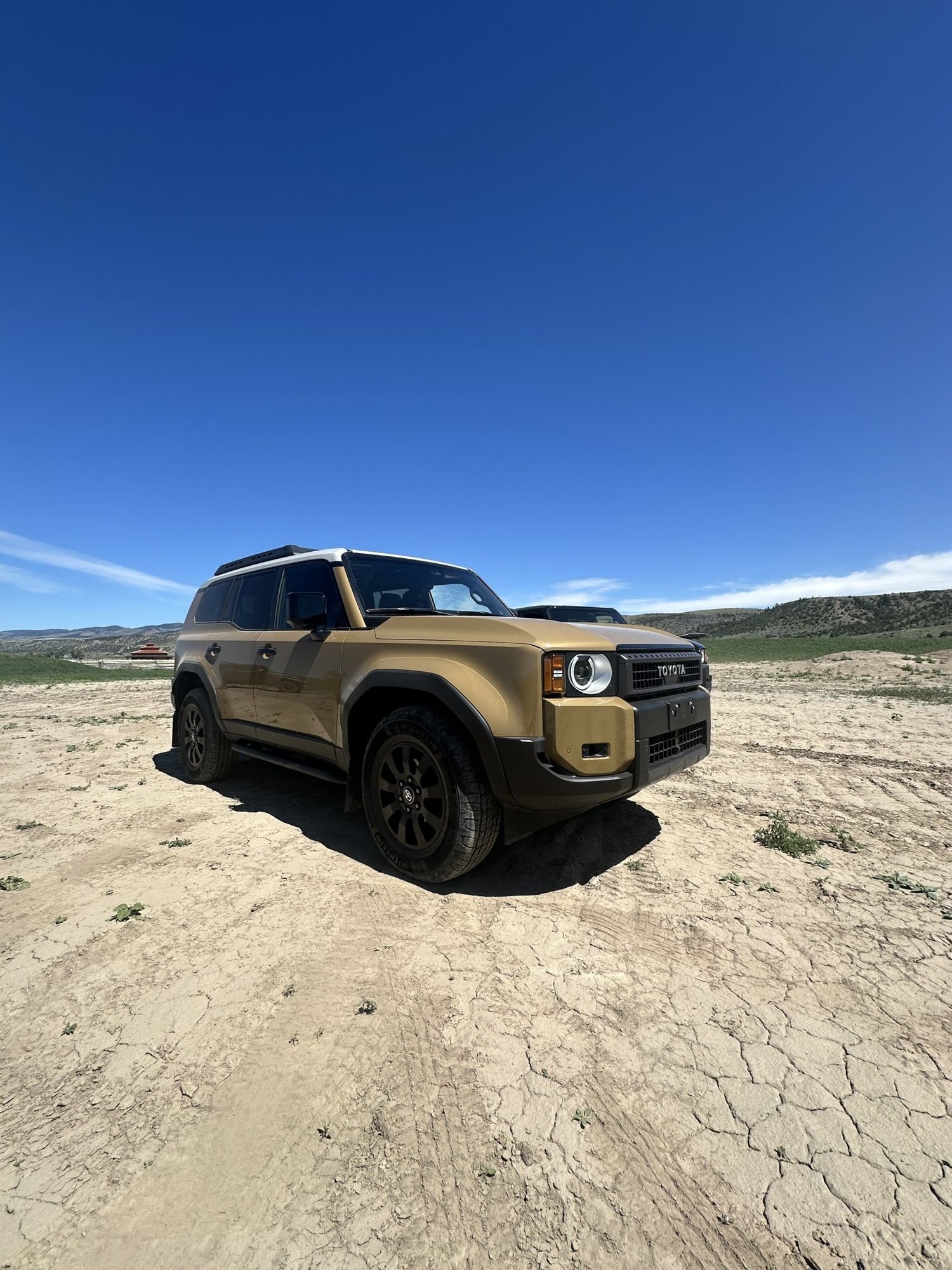 Front three-quarter view of a tan 2024 Land Cruiser with round headlights and TOYOTA grille lettering at XOverland Ranch near Bozeman, Montana
