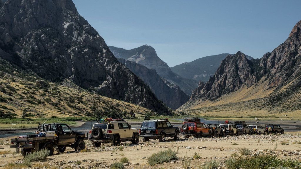 Line of off-road trucks parked beside the Clarks Fork River below steep canyon walls and jagged peaks on the Morrison Jeep Trail in Clarks Fork Canyon near Cody, Wyoming