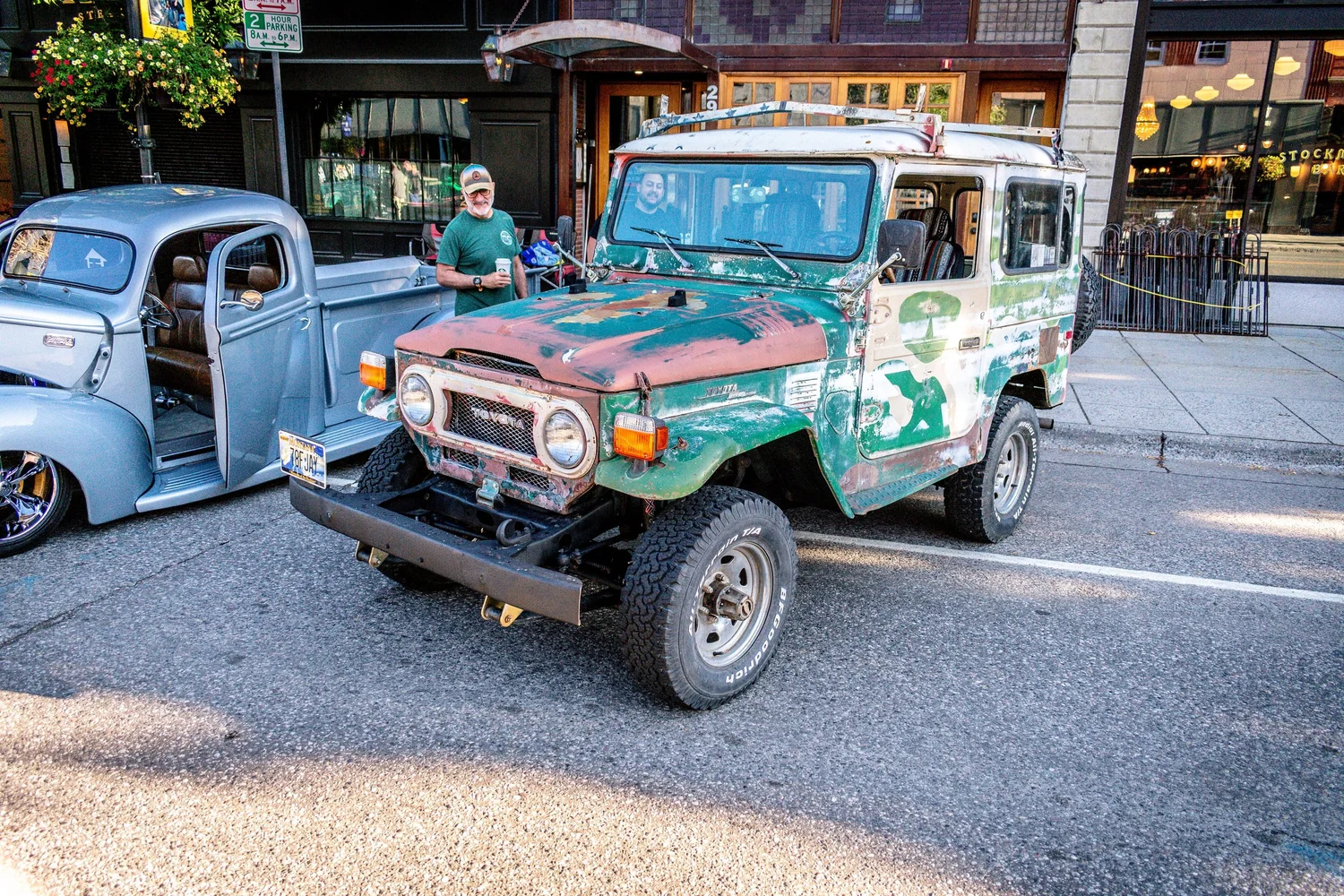 Green Toyota FJ40 Land Cruiser with camouflage paint parked at Cruisin on Main in Bozeman