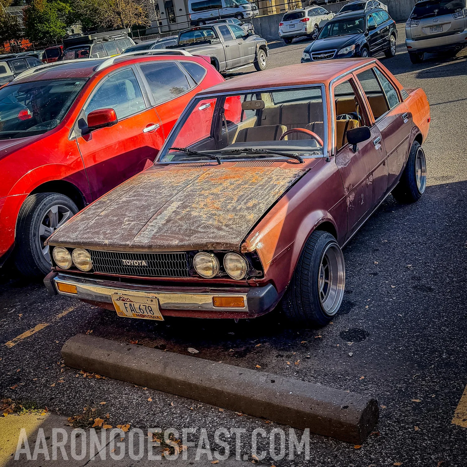 Patina-hood E70 Toyota Corolla sedan on polished deep-dish wheels in a parking lot