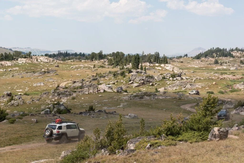 White Toyota FJ Cruiser driving through a granite-dotted plateau with a pond and trees on the Morrison Jeep Trail in Clarks Fork Canyon near Cody, Wyoming