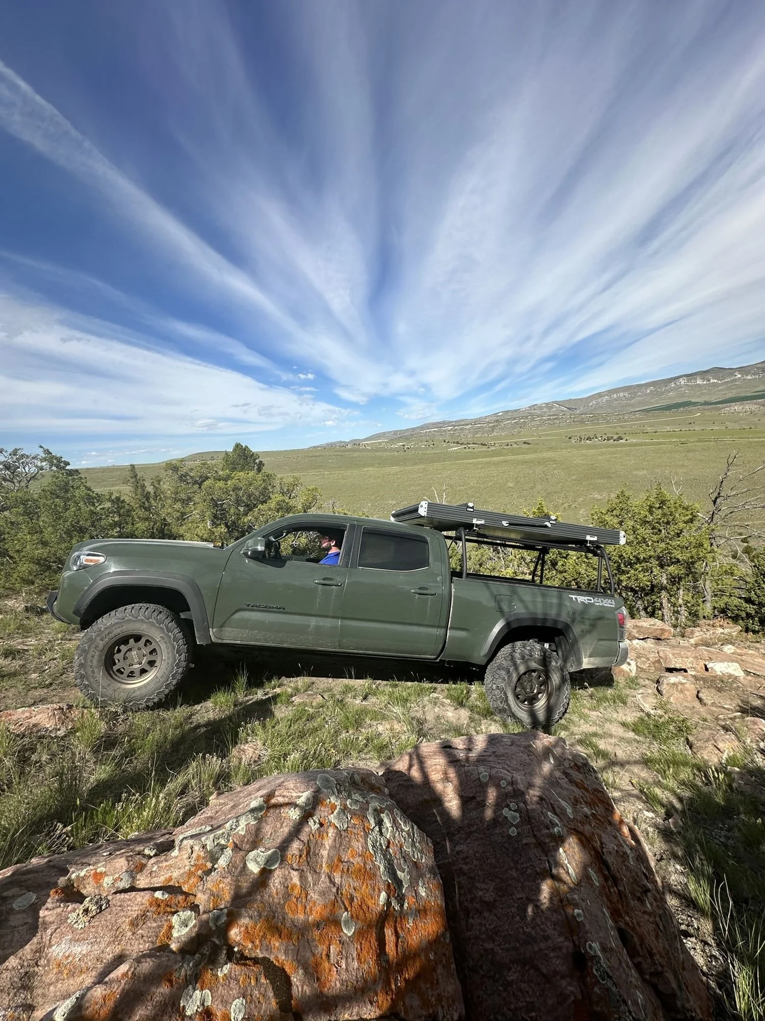 Green Toyota Tacoma with a rack crawling over rocks under a streaky sky at XOverland Ranch near Bozeman, Montana