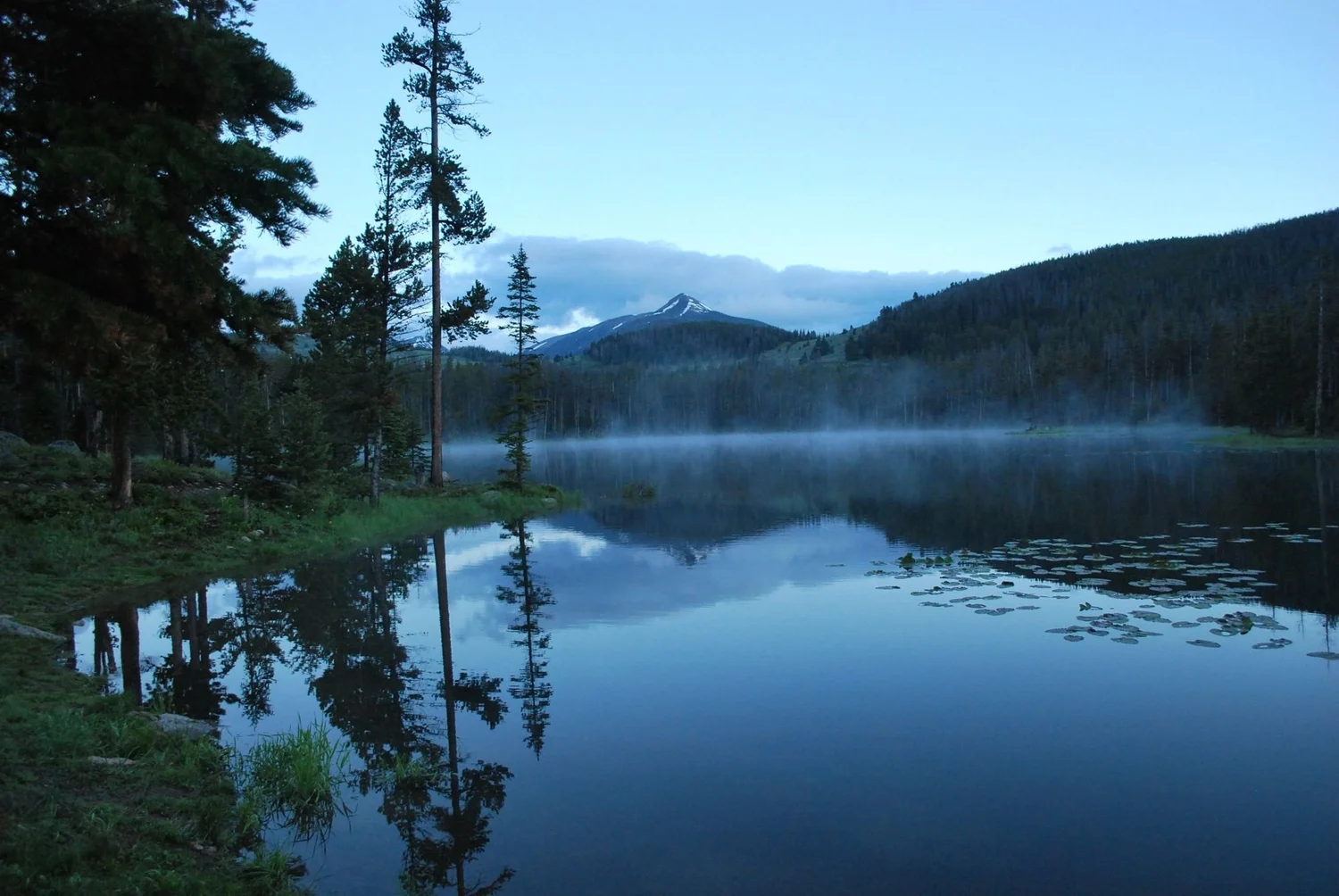 Still mountain lake with fog drifting across the water and pines reflected on the surface on the North Meadow Creek Twin Lakes trail in the Tobacco Root Mountains, Montana