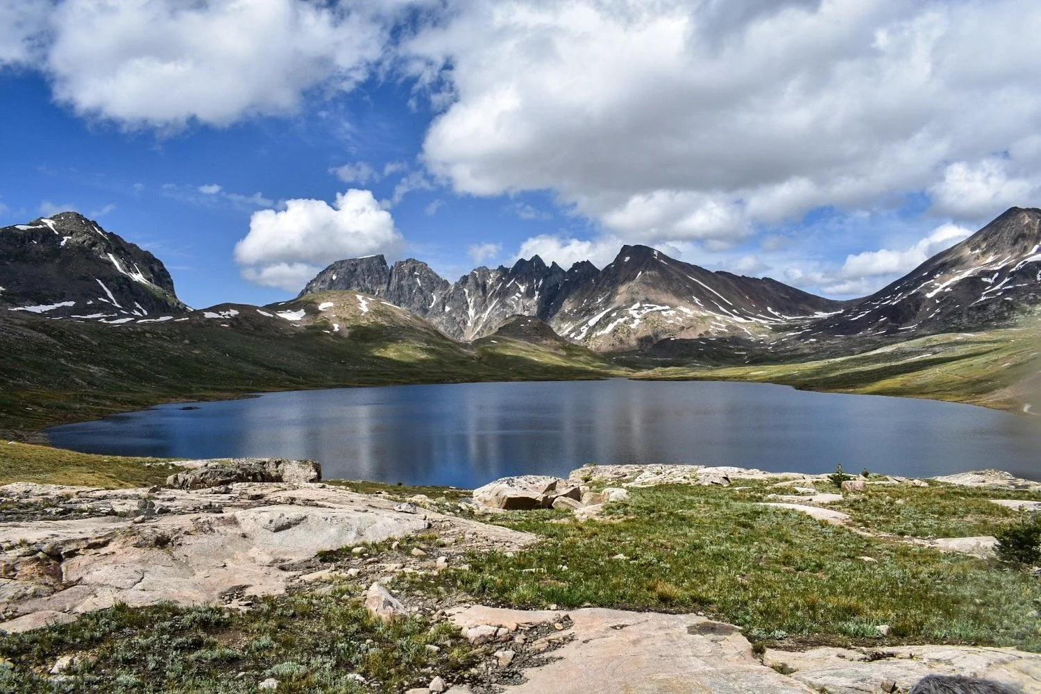 Wide alpine lake below a row of jagged peaks with granite slabs in the foreground near Cooke City, Montana