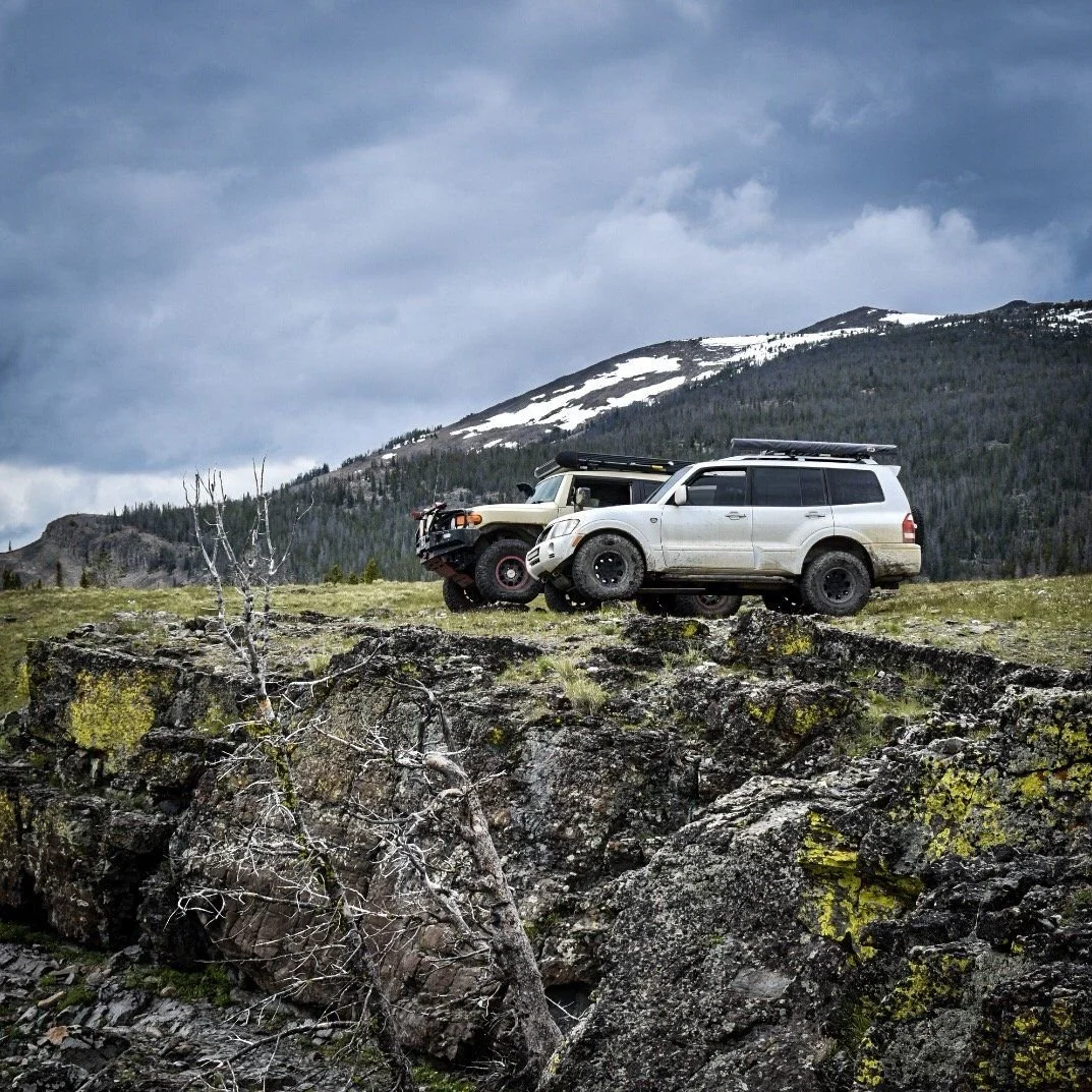 FJ Cruiser and a white SUV on a rocky ridge with a snowy peak behind in the Elkhorn Mountains near Boulder, Montana