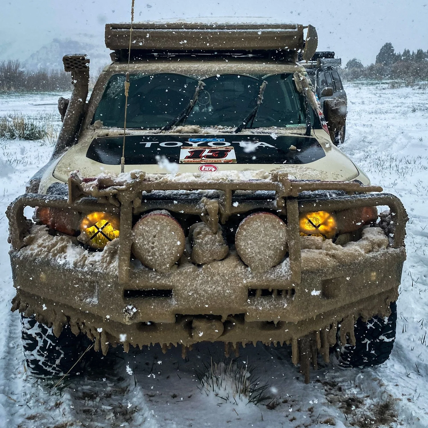 Mud-caked Toyota FJ Cruiser with icicles hanging from its steel bumper and lights in falling snow on a 406 Cruisers run in the upper Ruby River country, Montana