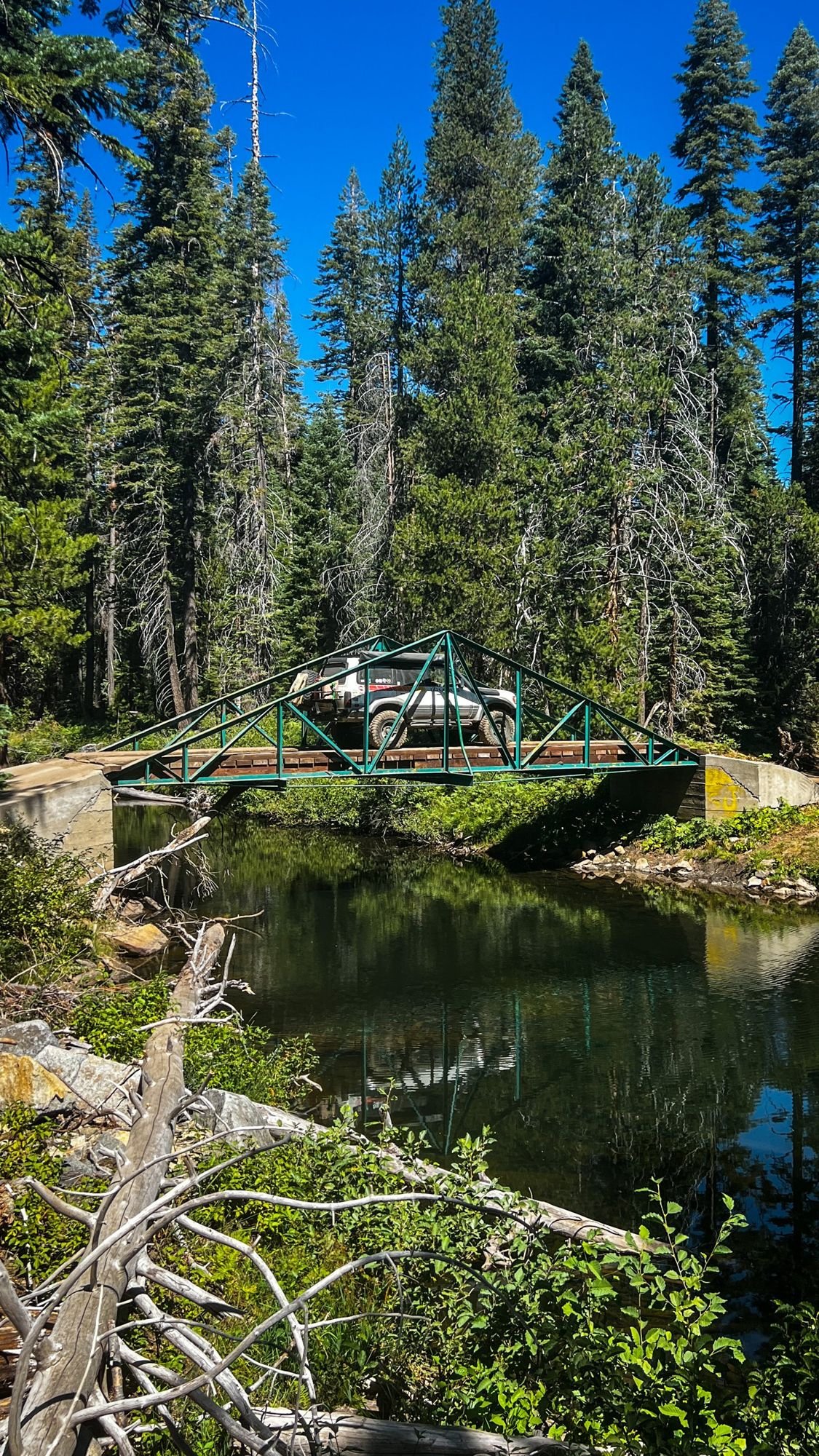 Green steel bridge over a calm river surrounded by pines on the Rubicon Trail in California during Rubithon 2022