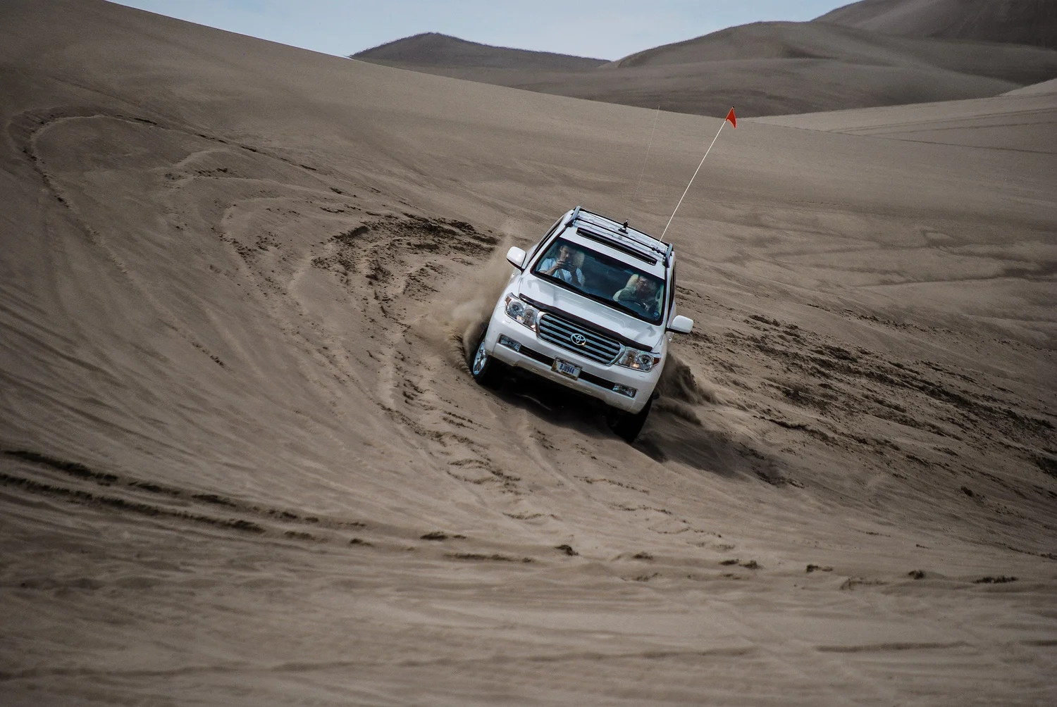 White Toyota Land Cruiser 200 Series powering up a sand bowl with sand spraying at the St. Anthony Sand Dunes in Idaho