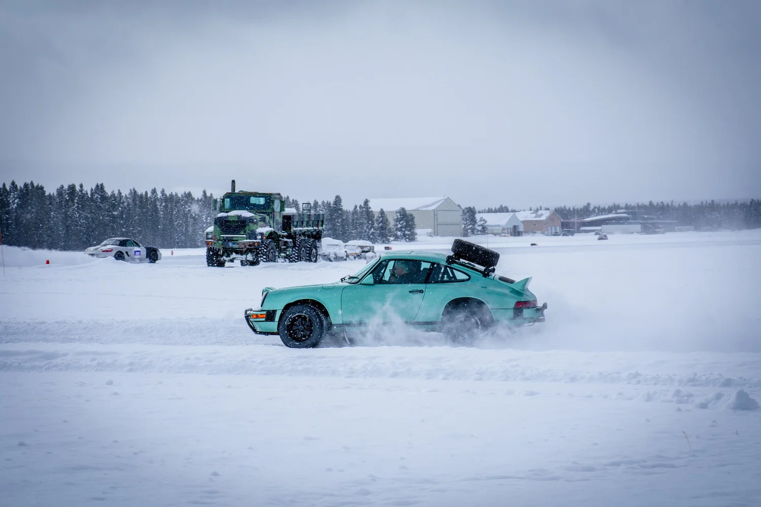 Teal Porsche 911 sliding across snow at the Frost and Furious ice races in West Yellowstone