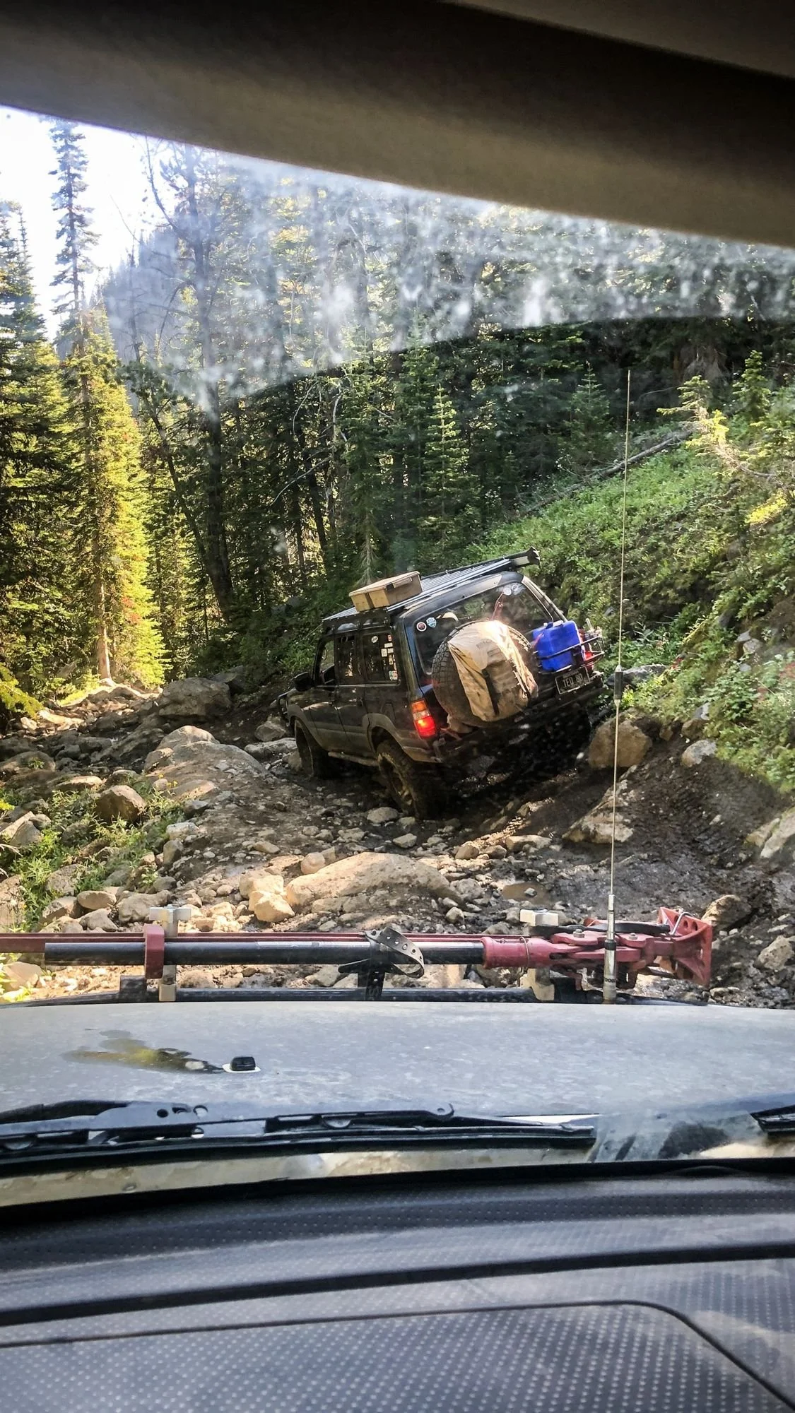 View over a hood of a Land Cruiser crawling a rocky ledge in the trees on the North Meadow Creek trail to McKelvey Lake in the Tobacco Root Mountains, Montana