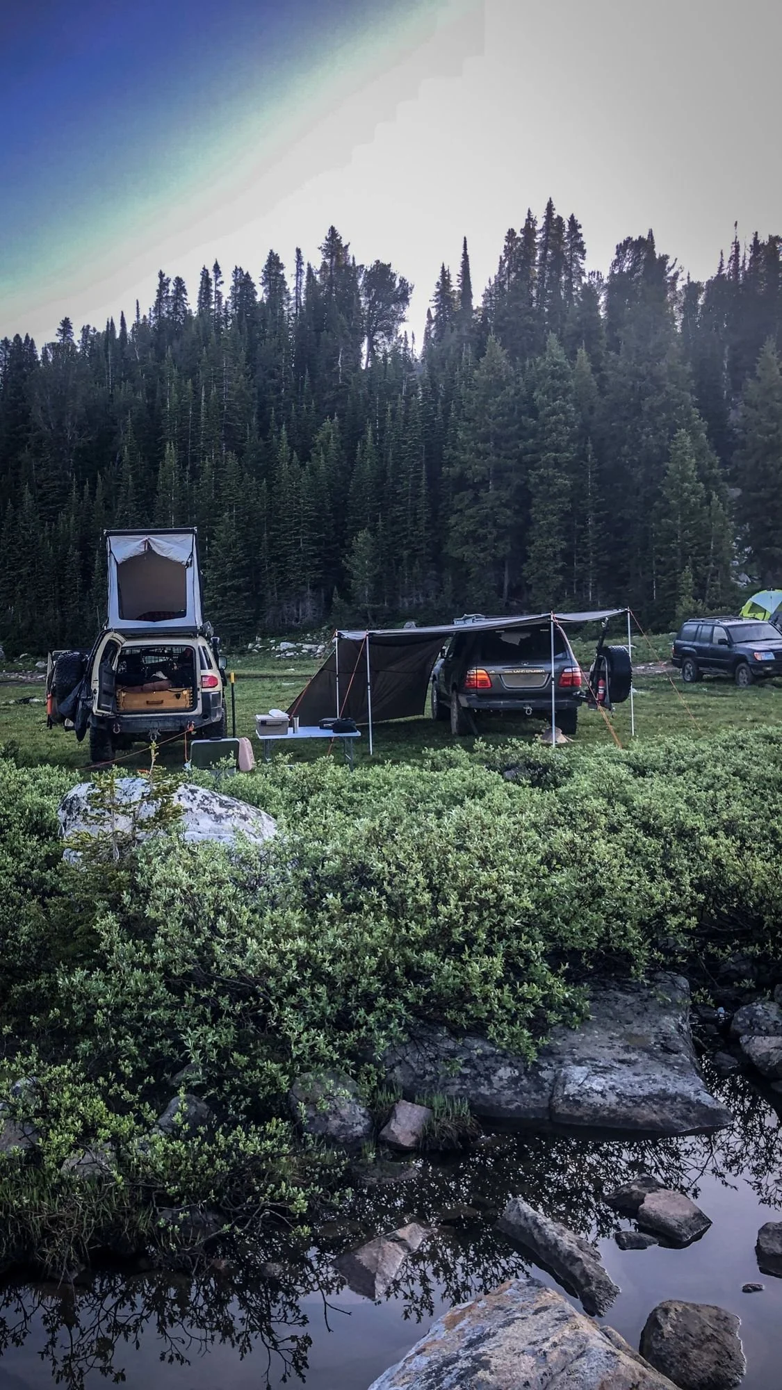 Camp in the trees with a rooftop tent and awning beside a small creek near Cooke City, Montana