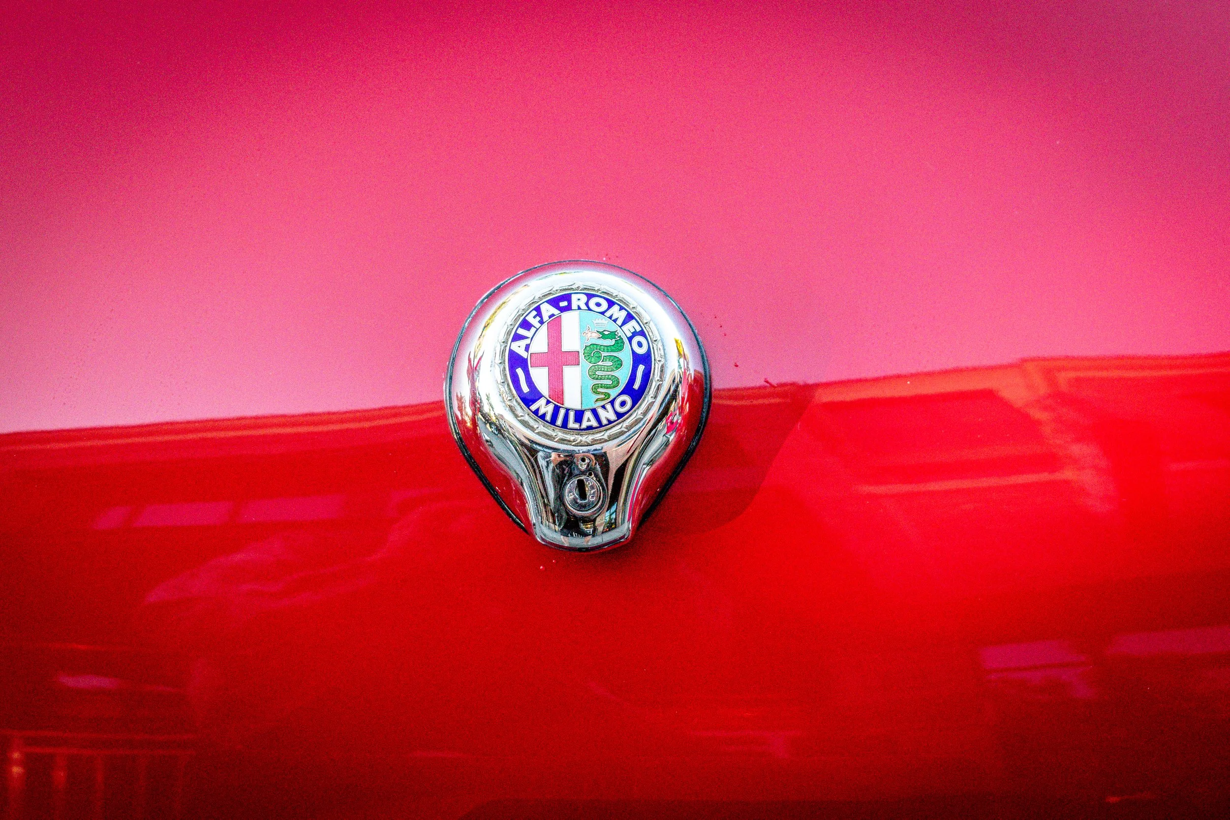 Close-up of the Alfa Romeo Milano hood ornament reflecting pink and red paint