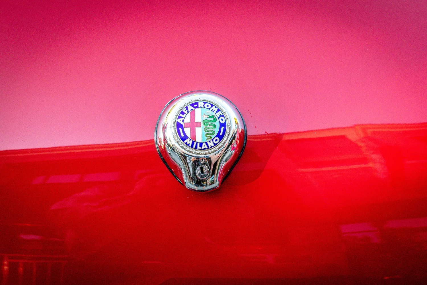 Close-up of the Alfa Romeo Milano hood ornament reflecting pink and red paint
