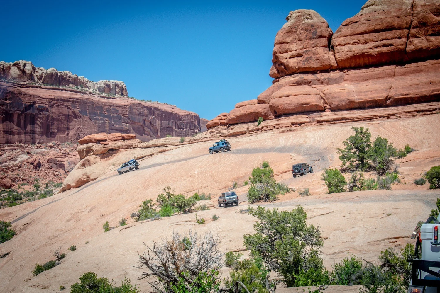 Six Land Cruisers strung across a slickrock bowl under red sandstone fins on the Seven Mile Rim trail near Moab, Utah