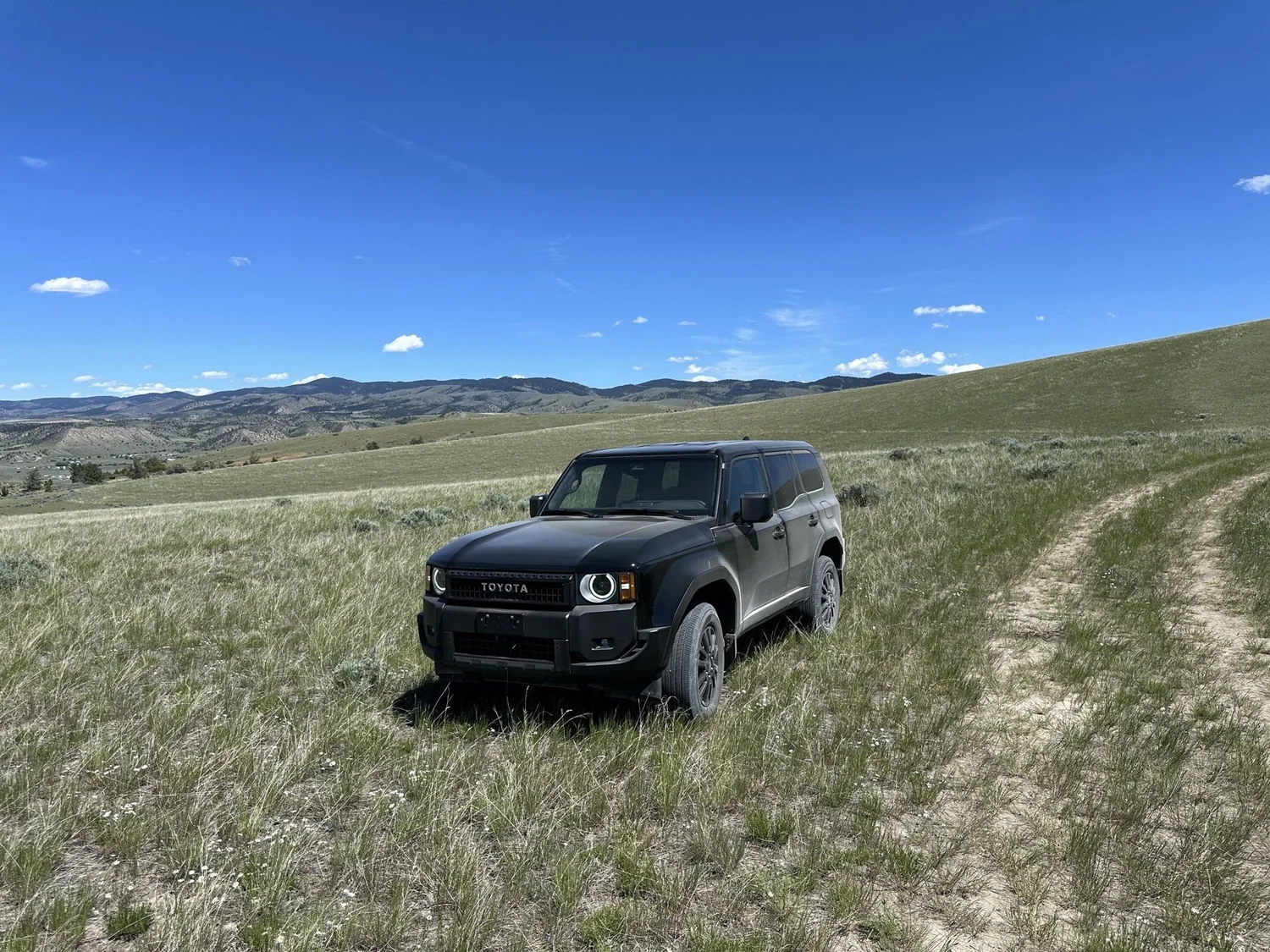 Black Land Cruiser 250 on a two-track through sagebrush with mountains behind at XOverland Ranch near Bozeman, Montana
