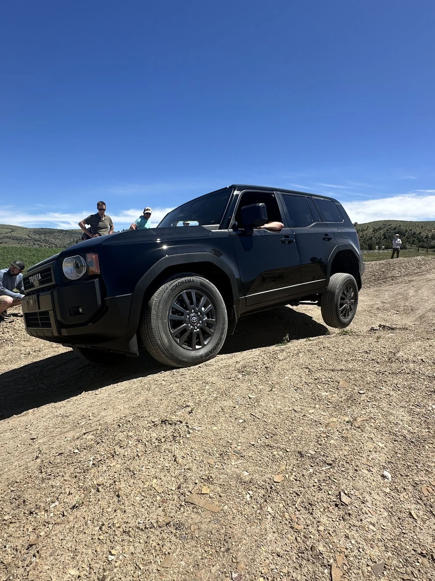 Black Land Cruiser 250 nose-up on a dirt mound with a driver at the wheel at XOverland Ranch near Bozeman, Montana