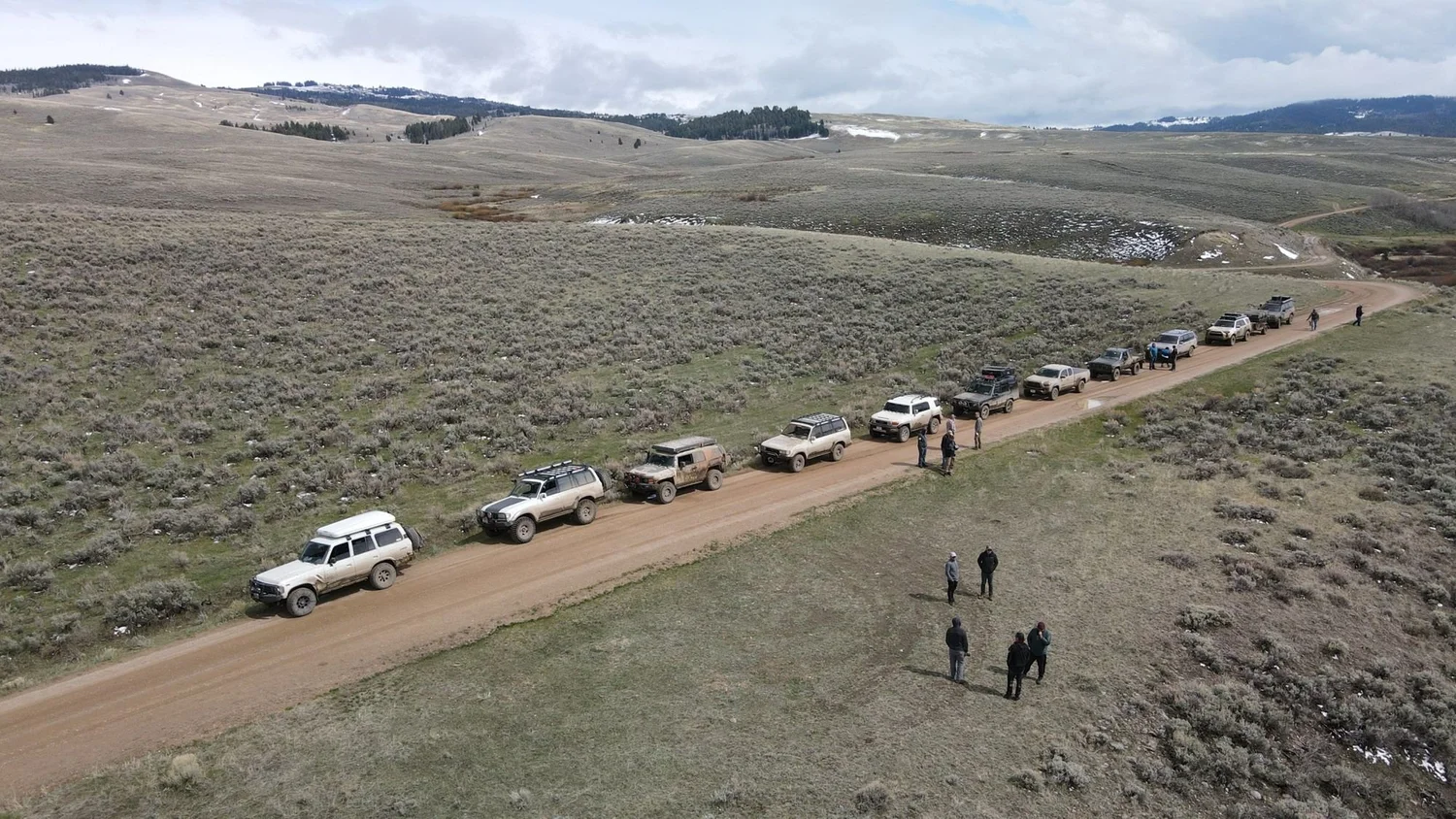 Drone view of a long line of Land Cruisers and other trucks parked along a dirt road through sagebrush hills on a 406 Cruisers run in the upper Ruby River country, Montana