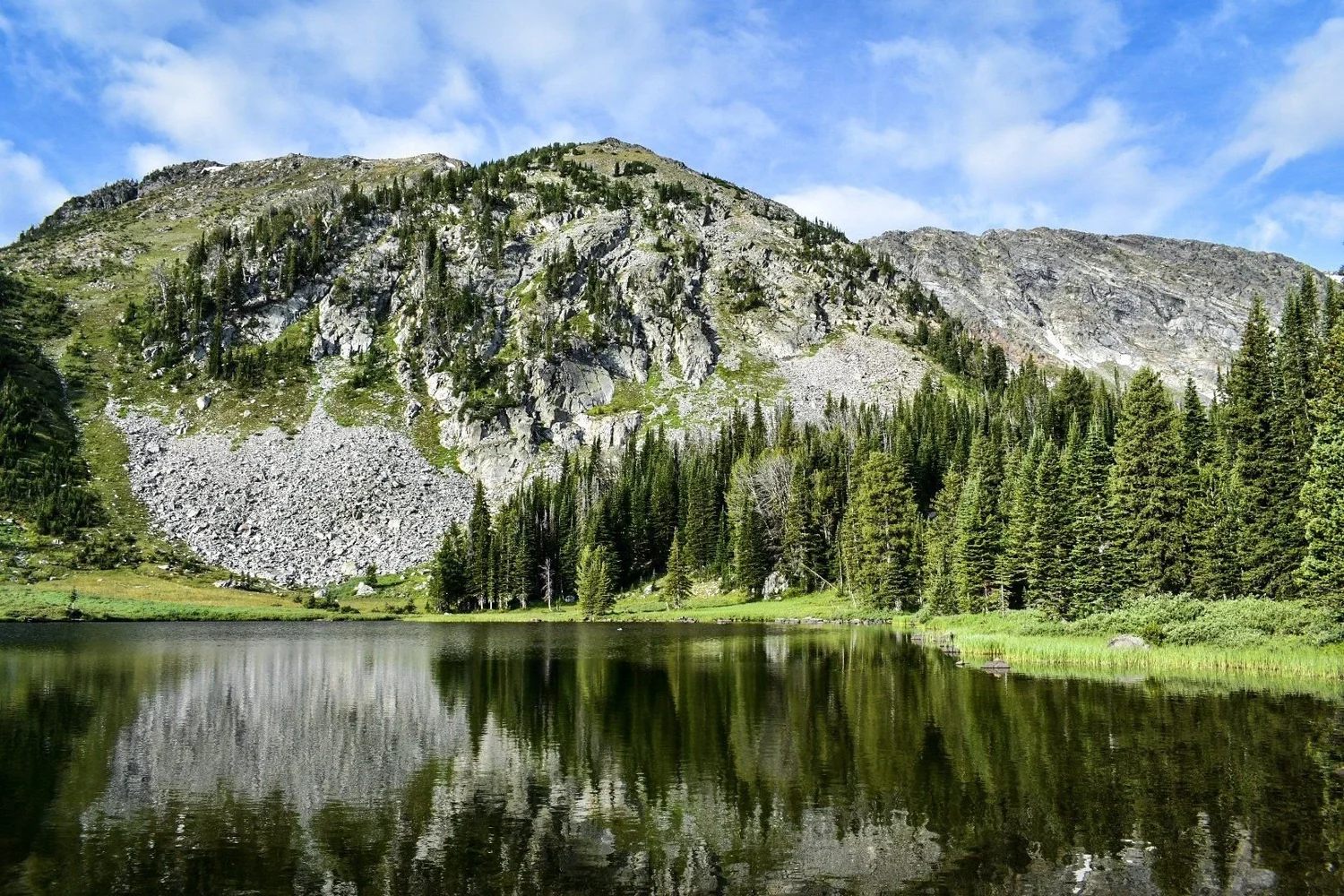 Talus slopes and forest reflected in a calm high lake on the North Meadow Creek trail to McKelvey Lake in the Tobacco Root Mountains, Montana