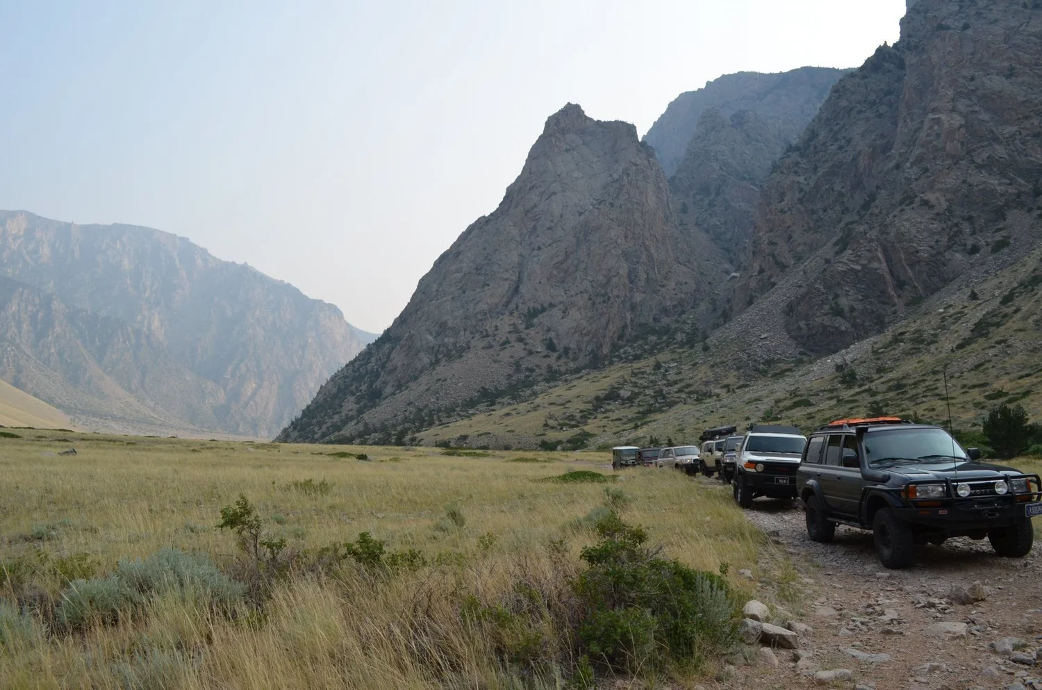 Line of trucks on a canyon road below a sharp rock peak on the Morrison Jeep Trail in Clarks Fork Canyon near Cody, Wyoming