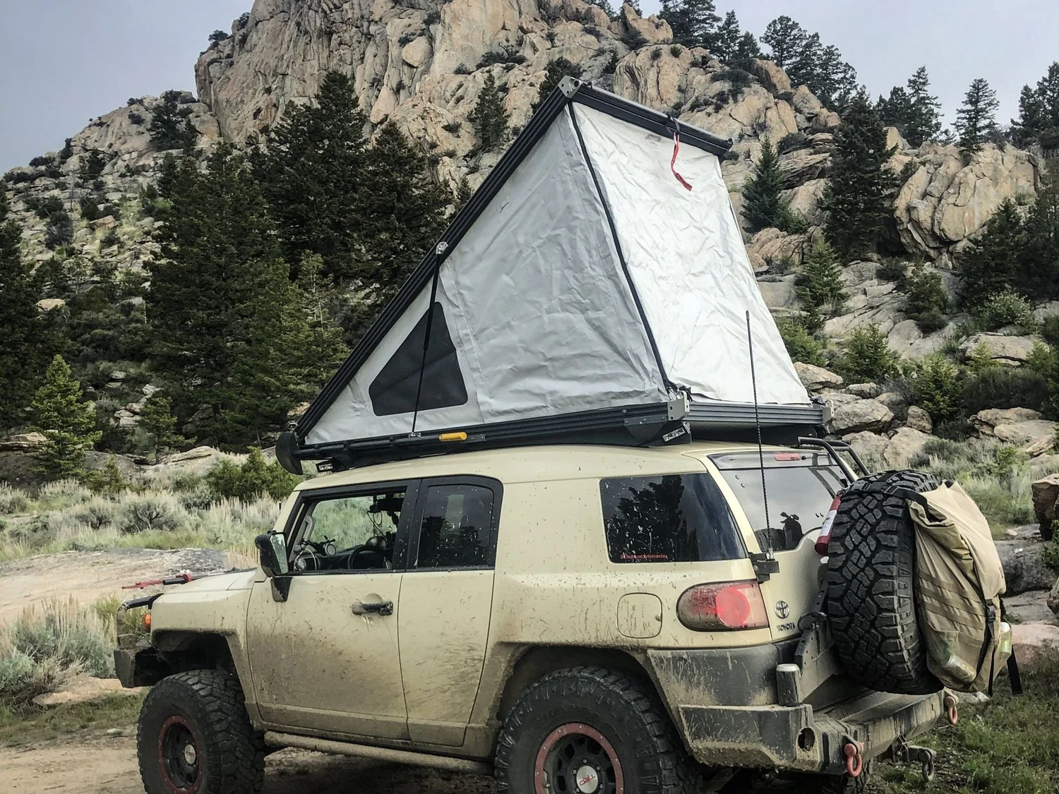 Tan Toyota FJ Cruiser with a pop-up rooftop tent below a tall granite dome on the Ringing Rocks trail near Pipestone, Montana