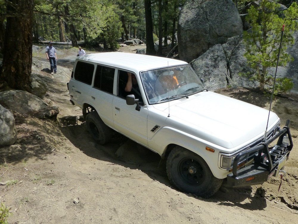 White Toyota Land Cruiser 60 Series with a bull bar on a rock step among granite boulders on the Ringing Rocks trail near Pipestone, Montana