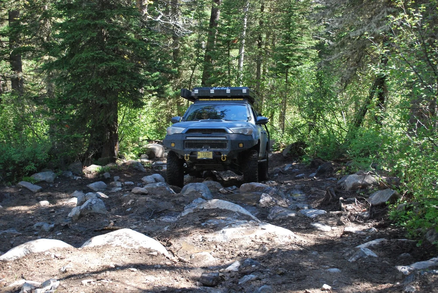 Blue 4Runner climbing over rocks on a forested trail on the North Meadow Creek Twin Lakes trail in the Tobacco Root Mountains, Montana