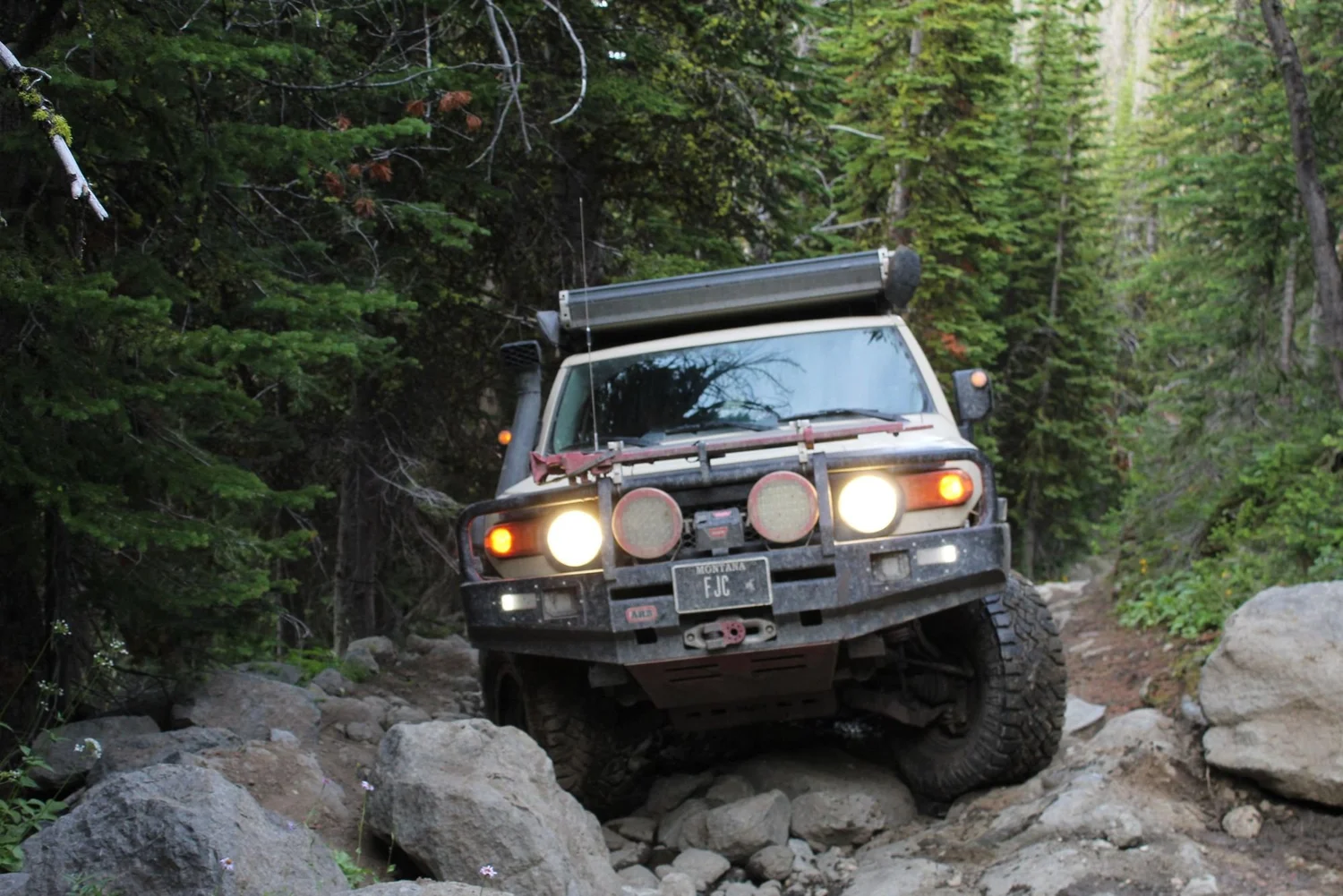 Tan FJ Cruiser with auxiliary lights crawling over a rock garden in the timber on the North Meadow Creek trail to McKelvey Lake in the Tobacco Root Mountains, Montana