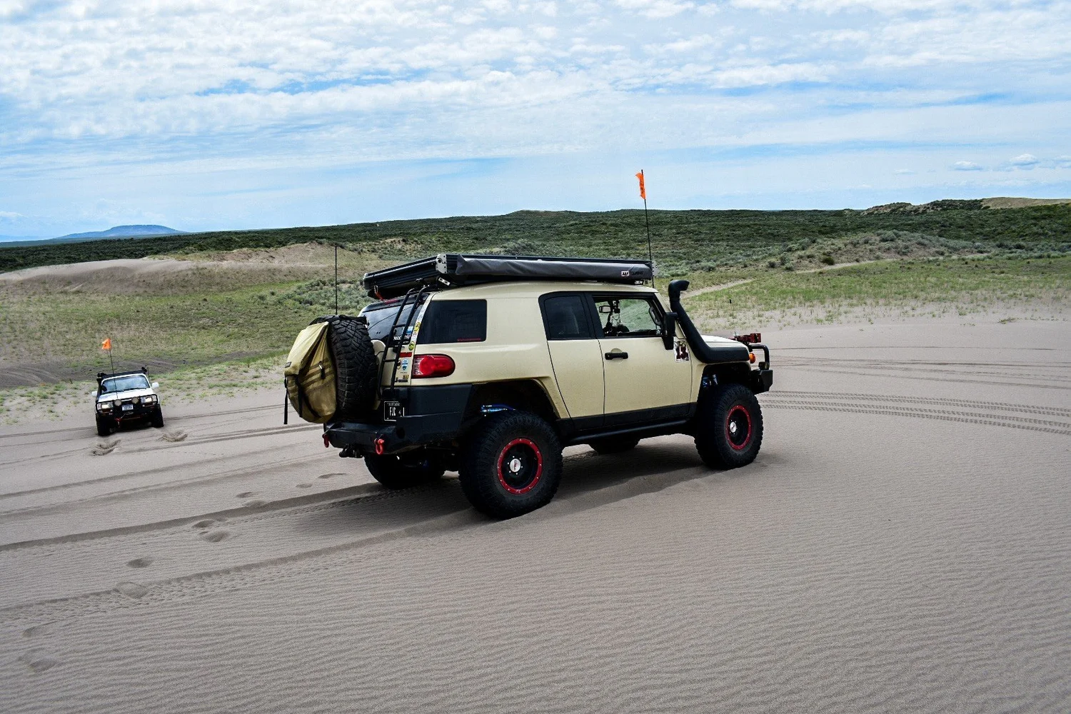 Tan Toyota FJ Cruiser with a snorkel, red wheels and a rooftop tent at the edge of the dunes at the St. Anthony Sand Dunes in Idaho