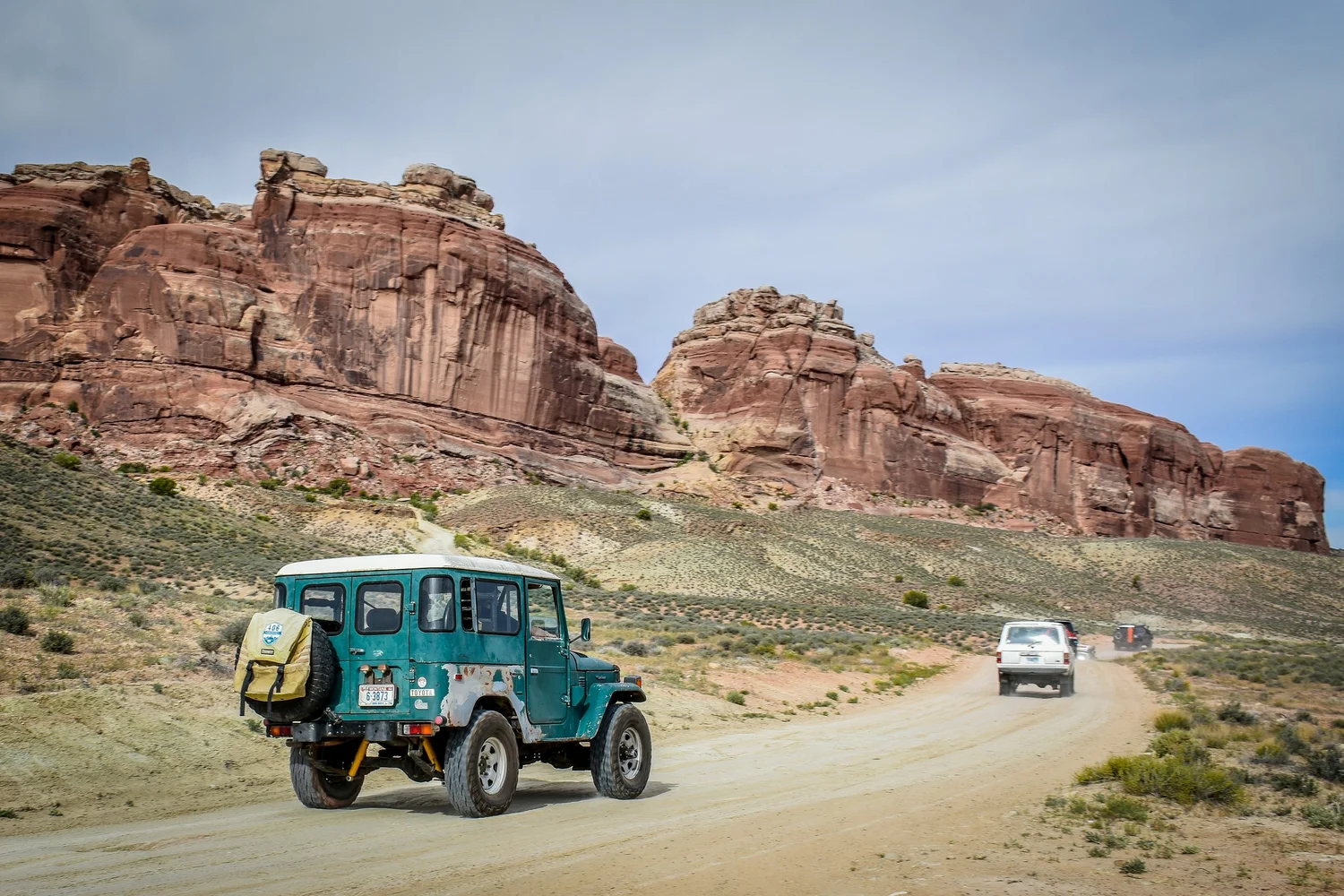Teal Toyota FJ40 Land Cruiser on a dirt road below red rock cliffs at Cruise Moab