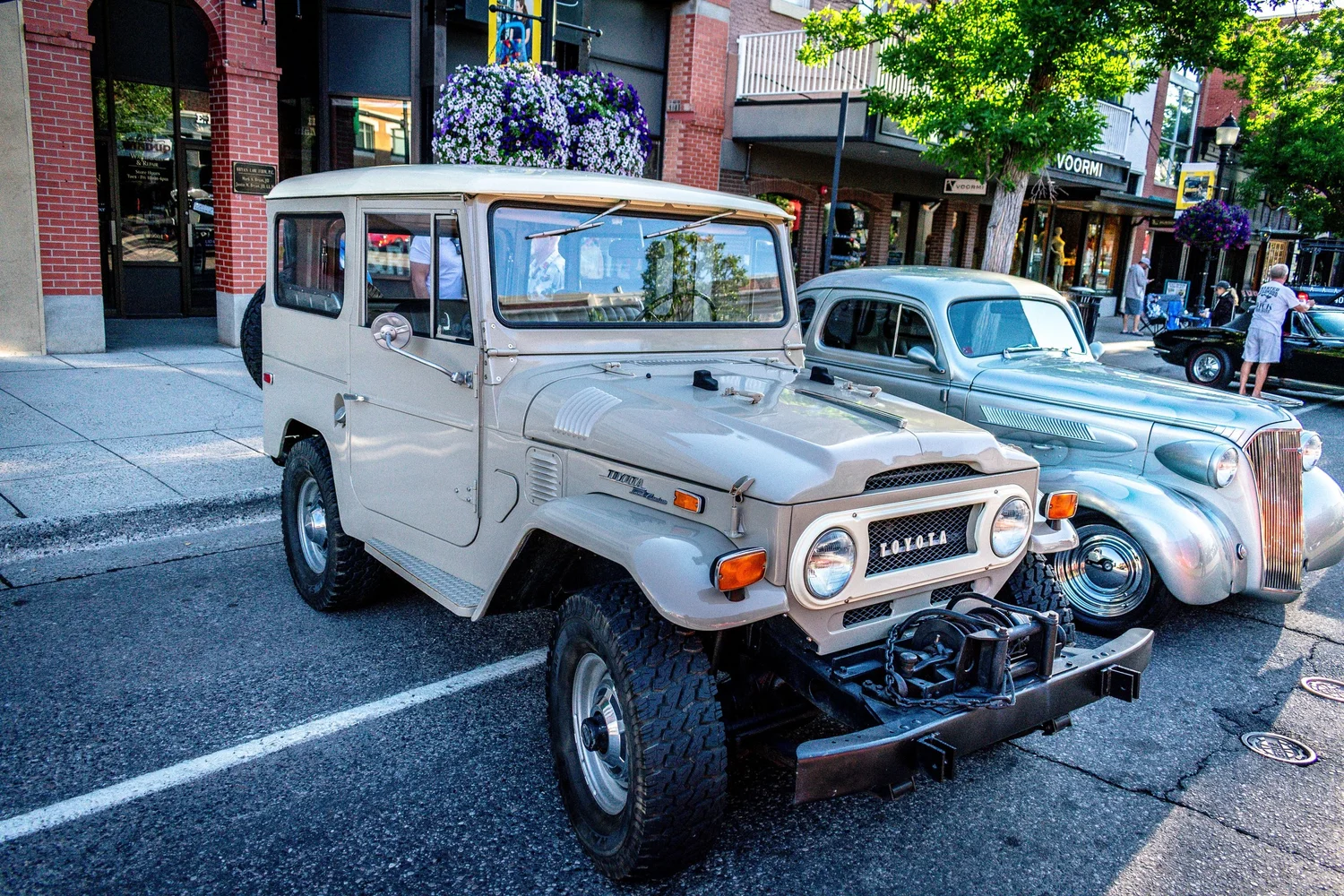 Tan Toyota FJ40 Land Cruiser parked beside a 1930s Chevrolet coupe at Cruisin on Main in Bozeman