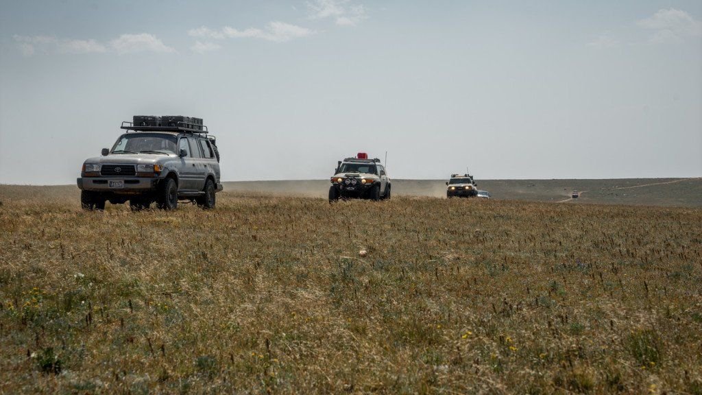 Gray Toyota Land Cruiser 80 Series leading a line of trucks across a wide grassy plateau on the Morrison Jeep Trail in Clarks Fork Canyon near Cody, Wyoming