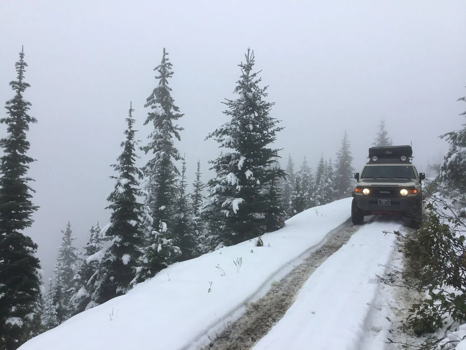 Tan FJ Cruiser on a narrow snowy road beside snow-covered brush on Little Bear Road in the Gallatin Range near Bozeman, Montana