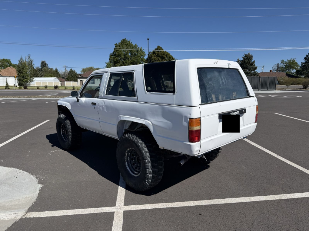 Rear three-quarter view of a white lifted 1985 Toyota 4Runner with a fiberglass top