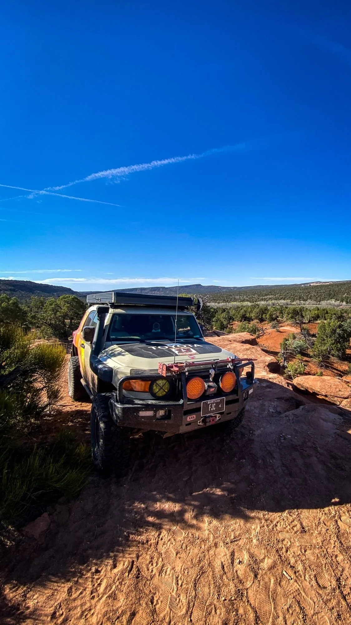 FJ Cruiser with lights on parked on slickrock under a clear blue morning sky on a spring road trip through Utah