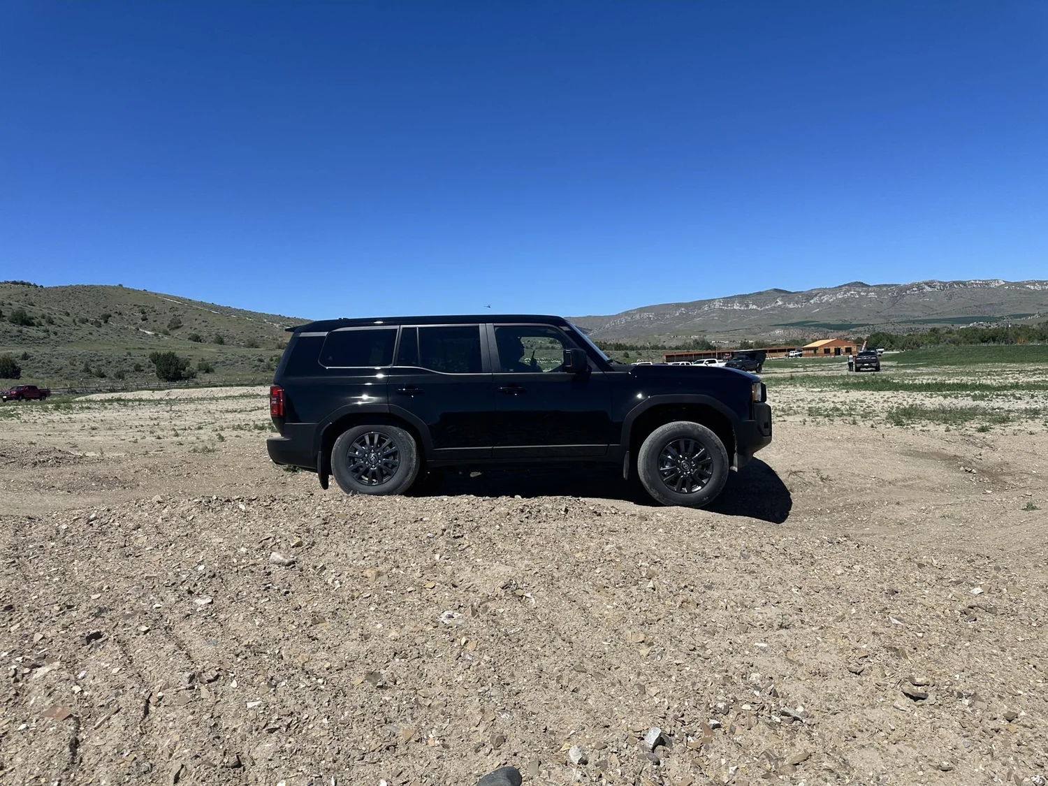 Black 2024 Toyota Land Cruiser side profile on a dirt practice area with hills behind at XOverland Ranch near Bozeman, Montana