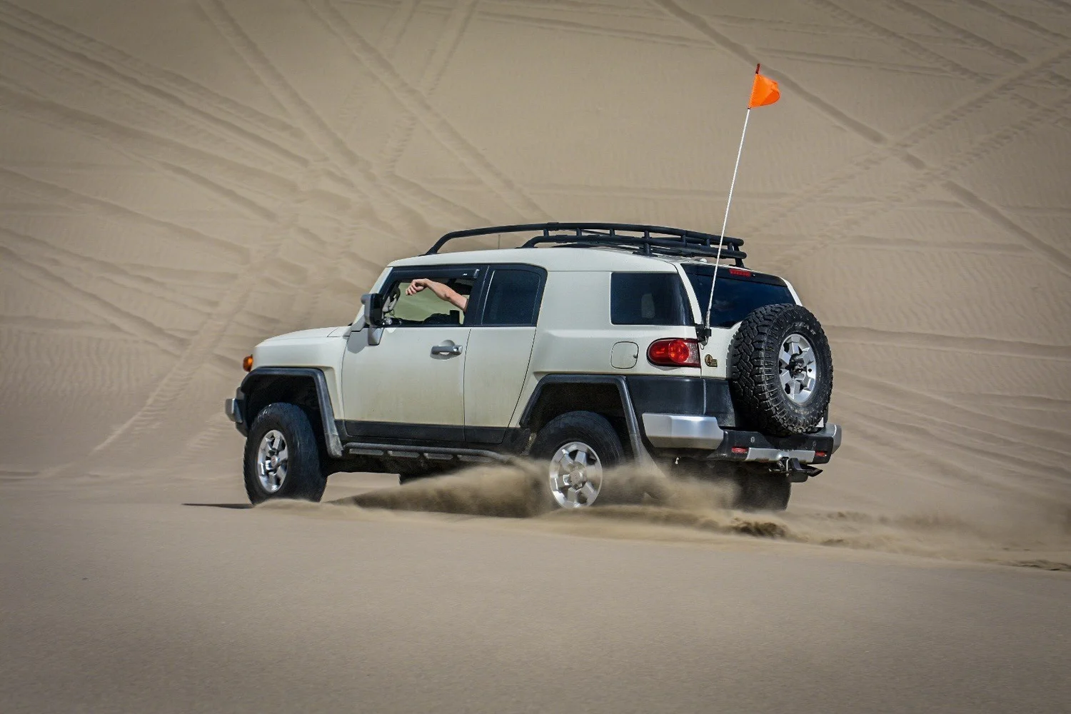 White Toyota FJ Cruiser throwing sand from its rear tires at the St. Anthony Sand Dunes in Idaho
