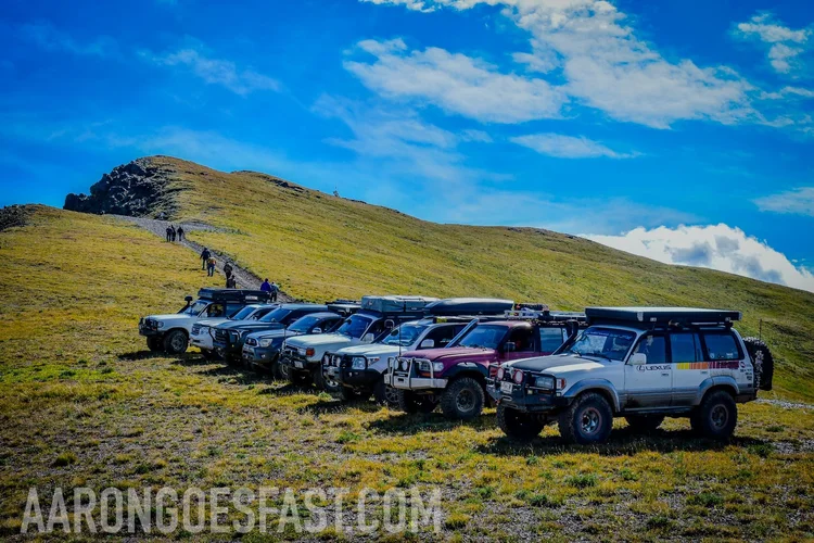 A line of Land Cruisers and trucks parked along a grassy ridge under a big sky near Cooke City, Montana