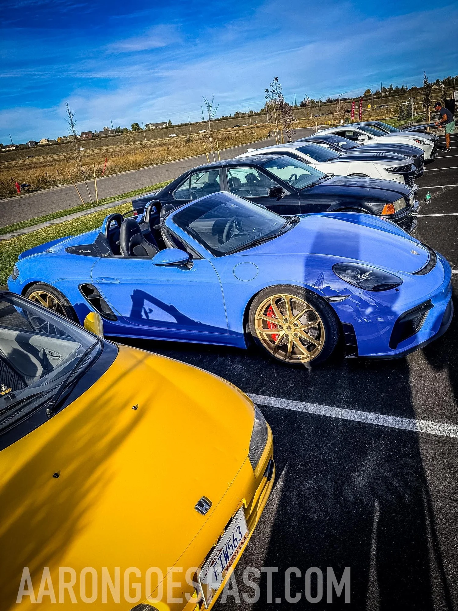 Blue Porsche 718 Spyder with gold wheels parked next to the yellow Honda Beat