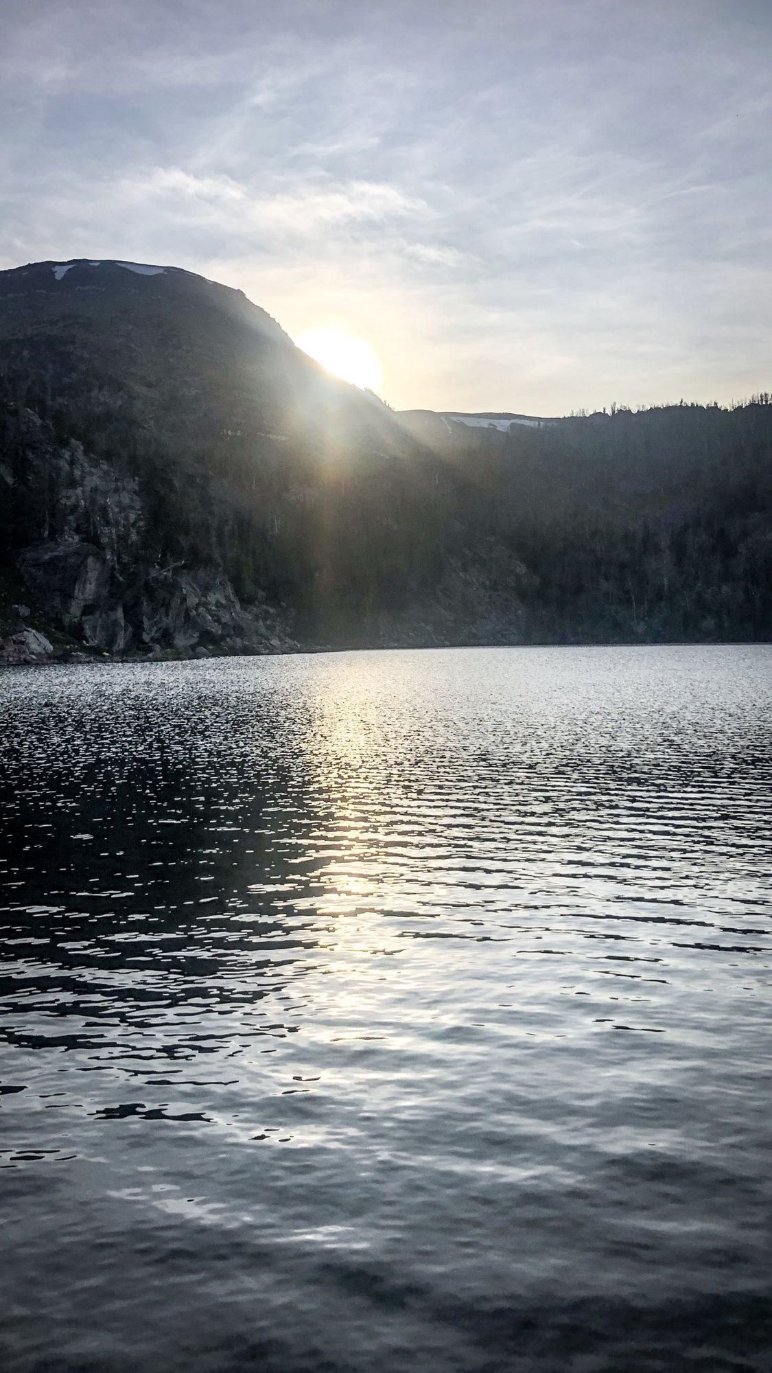 Sun rising over a ridge above a rippling mountain lake on the North Meadow Creek trail to McKelvey Lake in the Tobacco Root Mountains, Montana