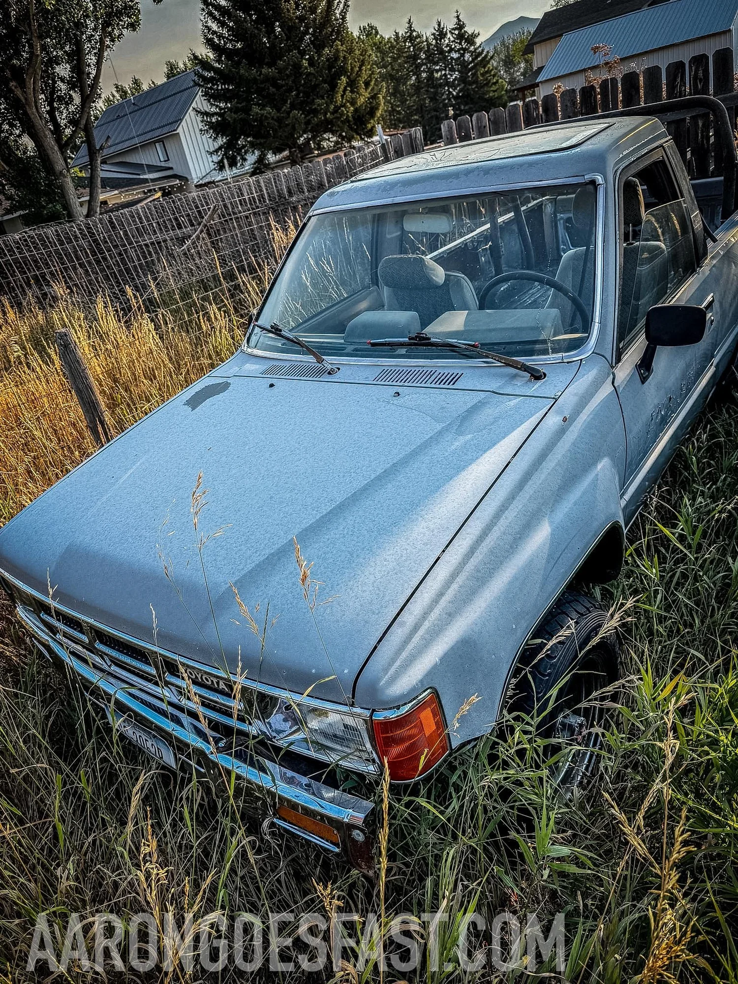 Light blue first-generation Toyota 4Runner in tall grass behind a wooden fence