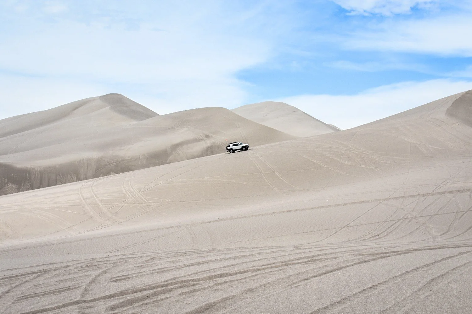 A single small white SUV dwarfed by tall tracked dune peaks at the St. Anthony Sand Dunes in Idaho