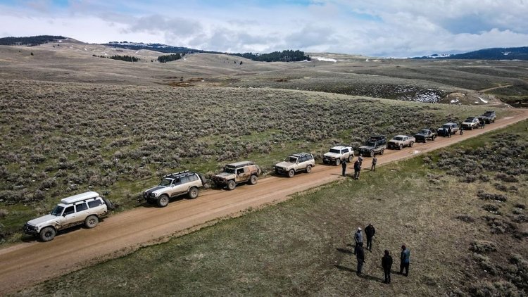 A line of Toyota Land Cruisers parked along a wide graded dirt road through sagebrush on the Dillon club run.
