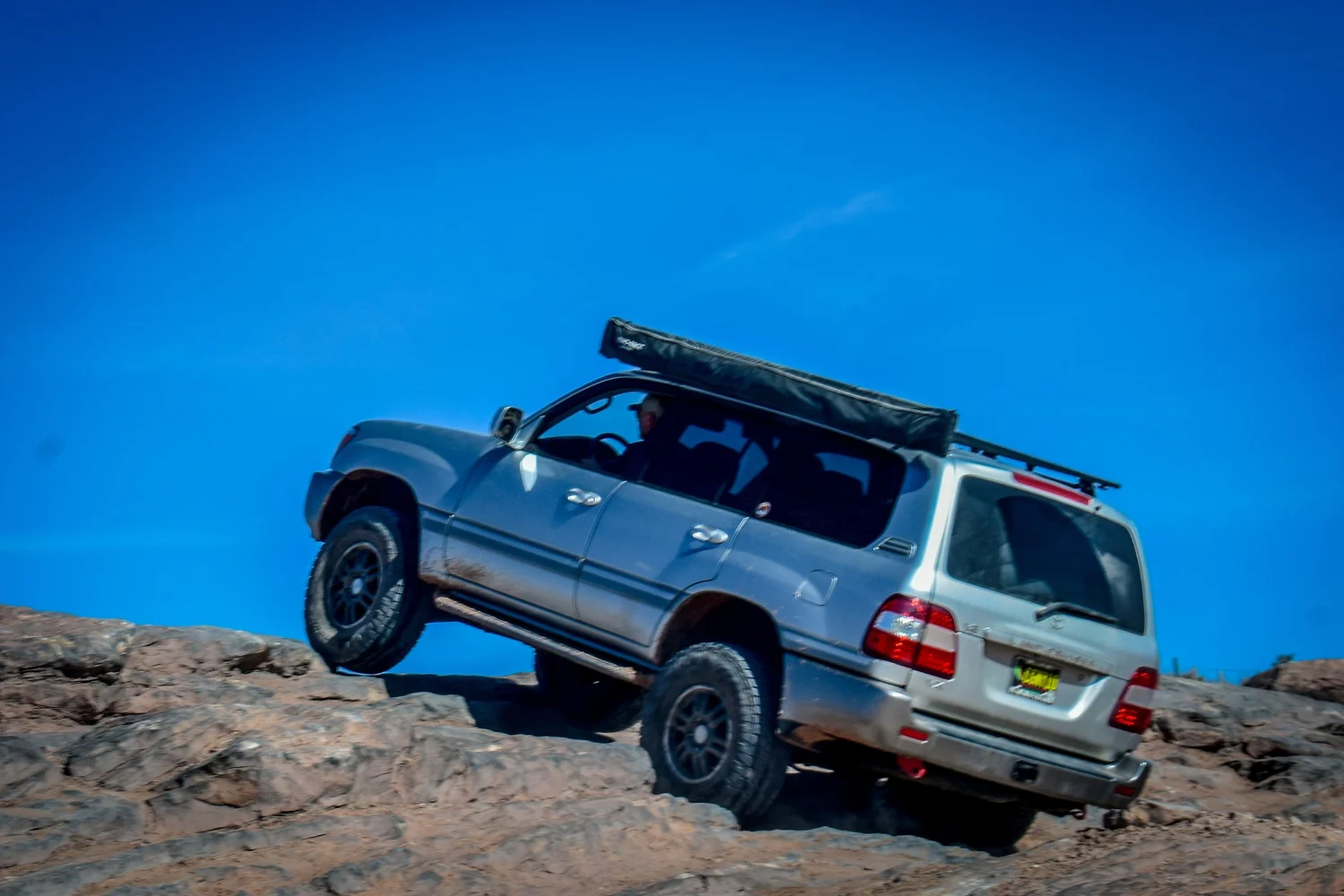 Silver 100 Series Toyota Land Cruiser with a roof rack climbing slickrock at Cruise Moab