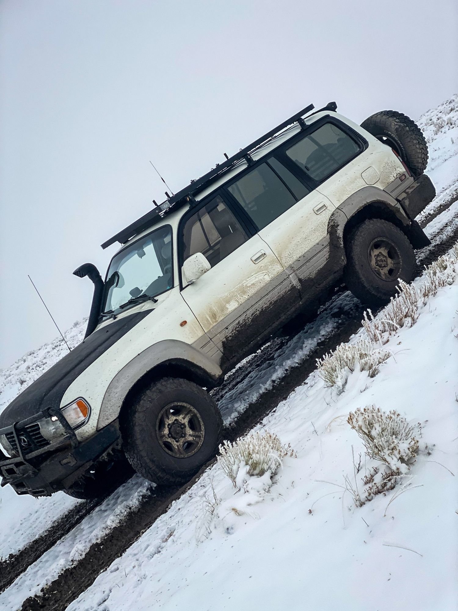 White Toyota Land Cruiser with a snorkel tilted hard on an off-camber snowy slope on a 406 Cruisers run in the upper Ruby River country, Montana