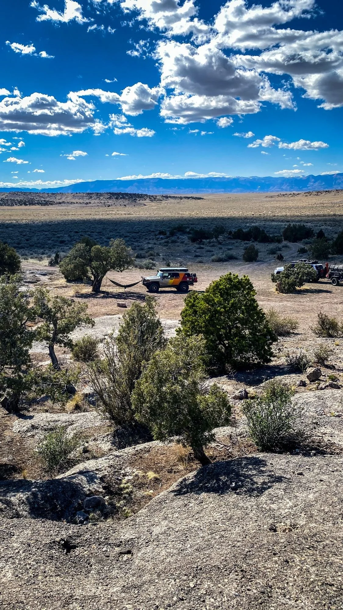 Wide desert overlook with junipers and a truck in the distance under big clouds on a spring road trip through Utah